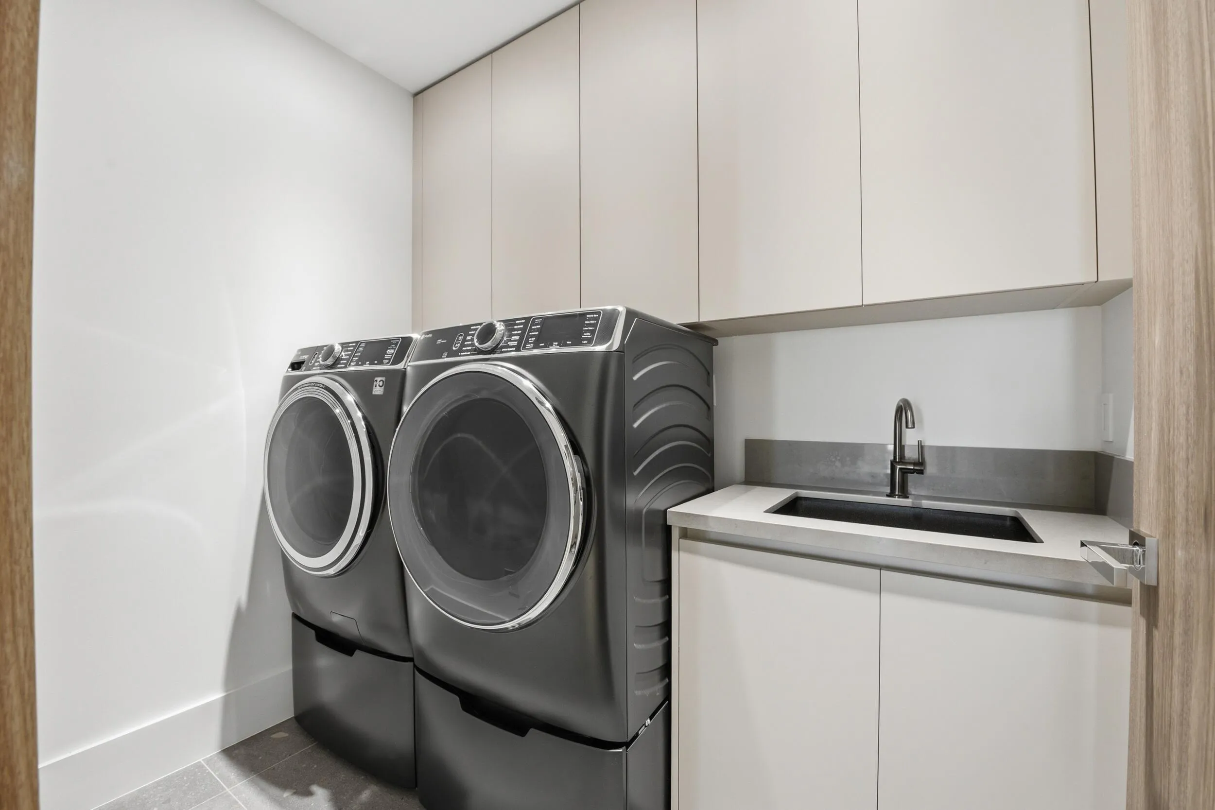 Integrated laundry appliances, built-in cabinetry, under-mount sink, matte black faucet, and light-toned countertop