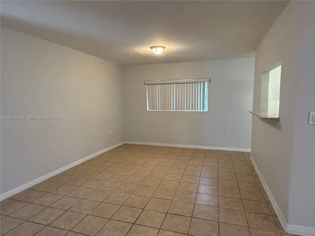 Neutral-toned interior space featuring ceramic tile flooring, a window equipped with vertical blinds, and a pass-through opening with a ledge