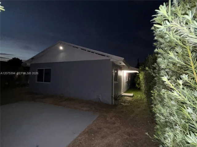 Stucco exterior featuring a concrete driveway and mature perimeter landscaping