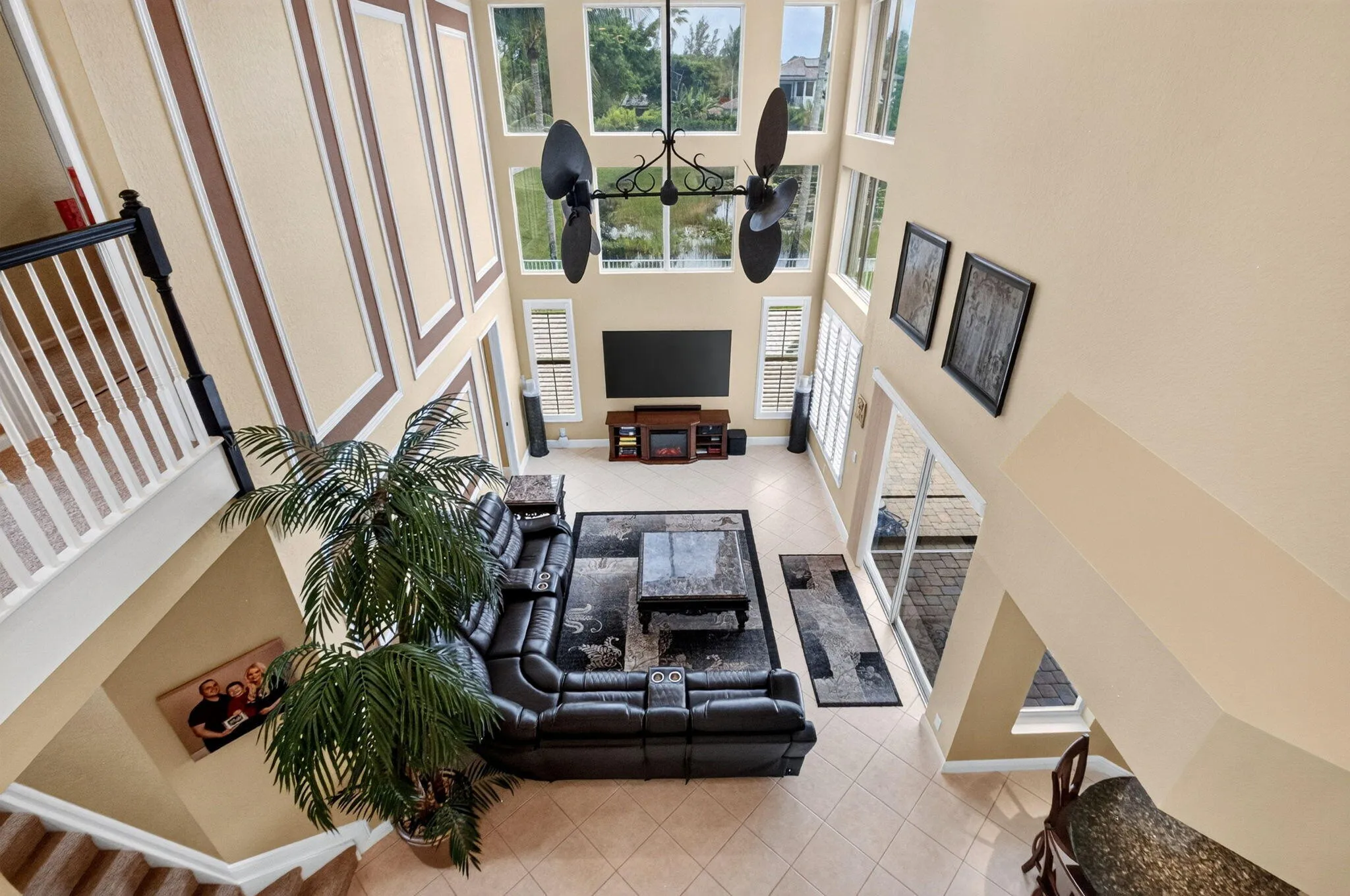 Two-story living room with a tiered window arrangement, decorative wall molding, a ceiling fan with integrated lighting, and tile flooring