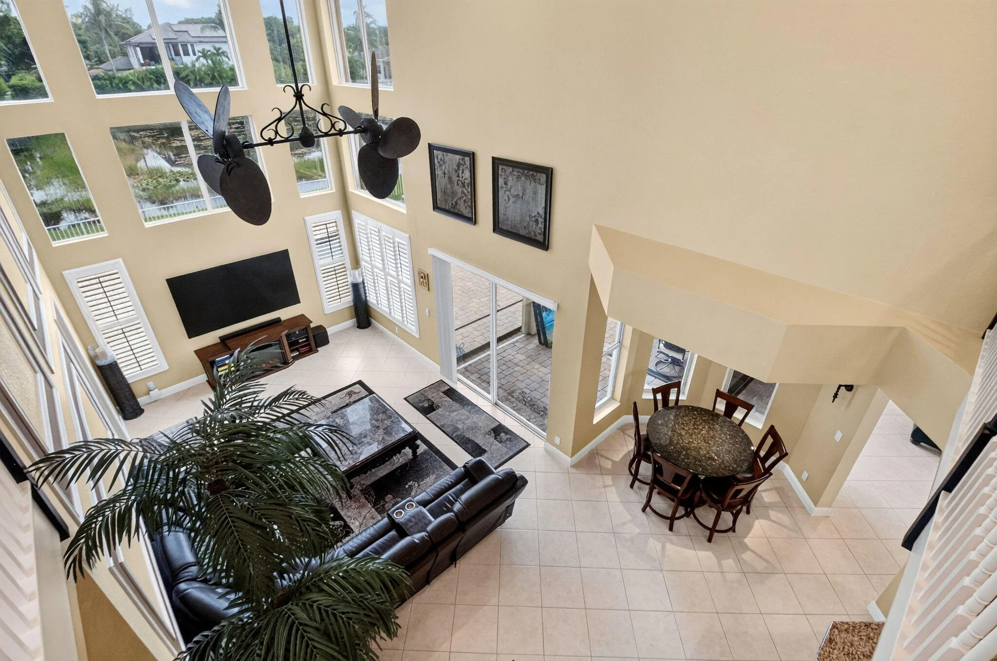 Two-story living area with high ceilings, multiple windows, tile flooring, and a decorative ceiling fan