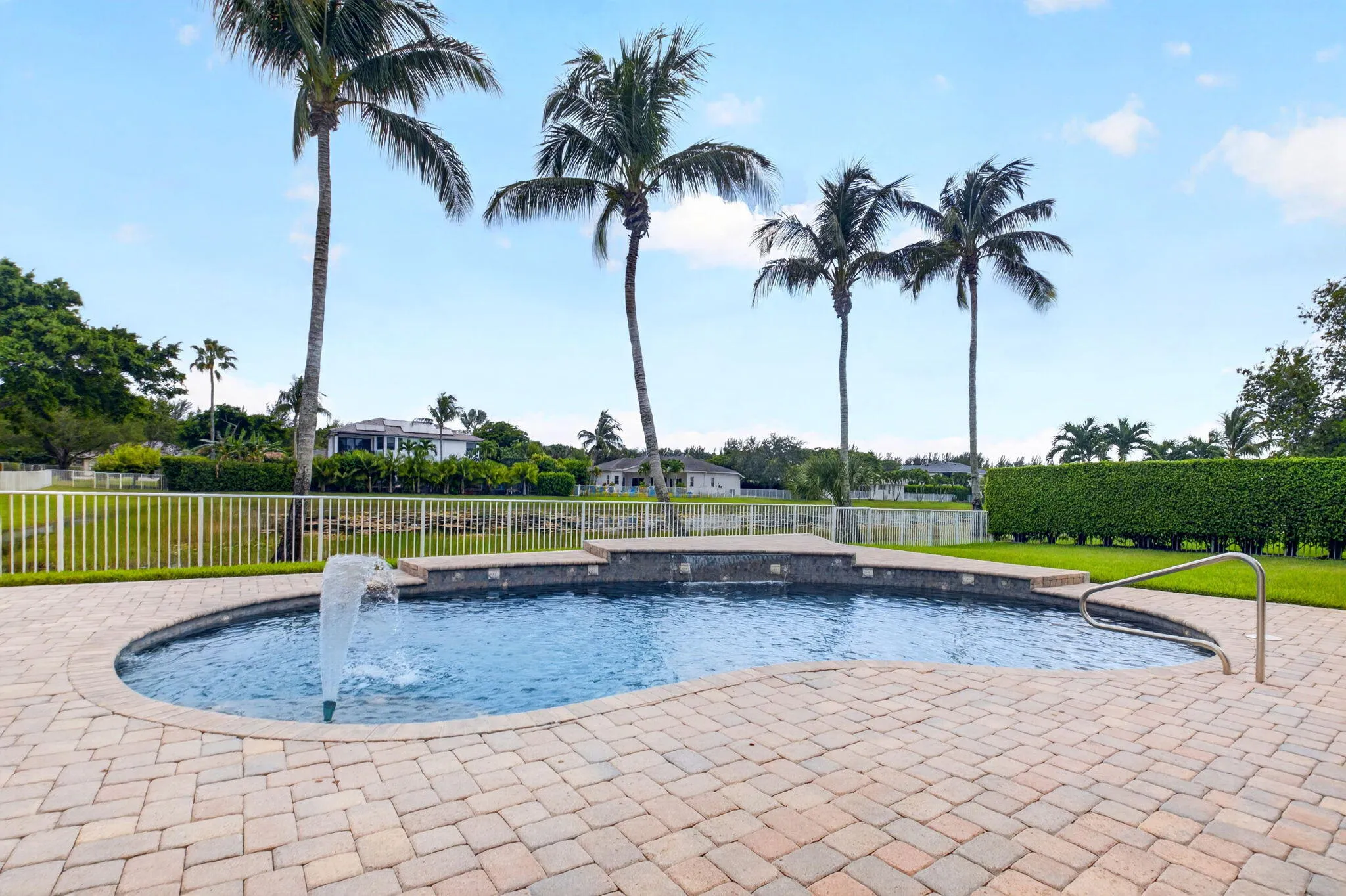 Freeform swimming pool with a fountain feature, surrounded by paver decking and a green lawn