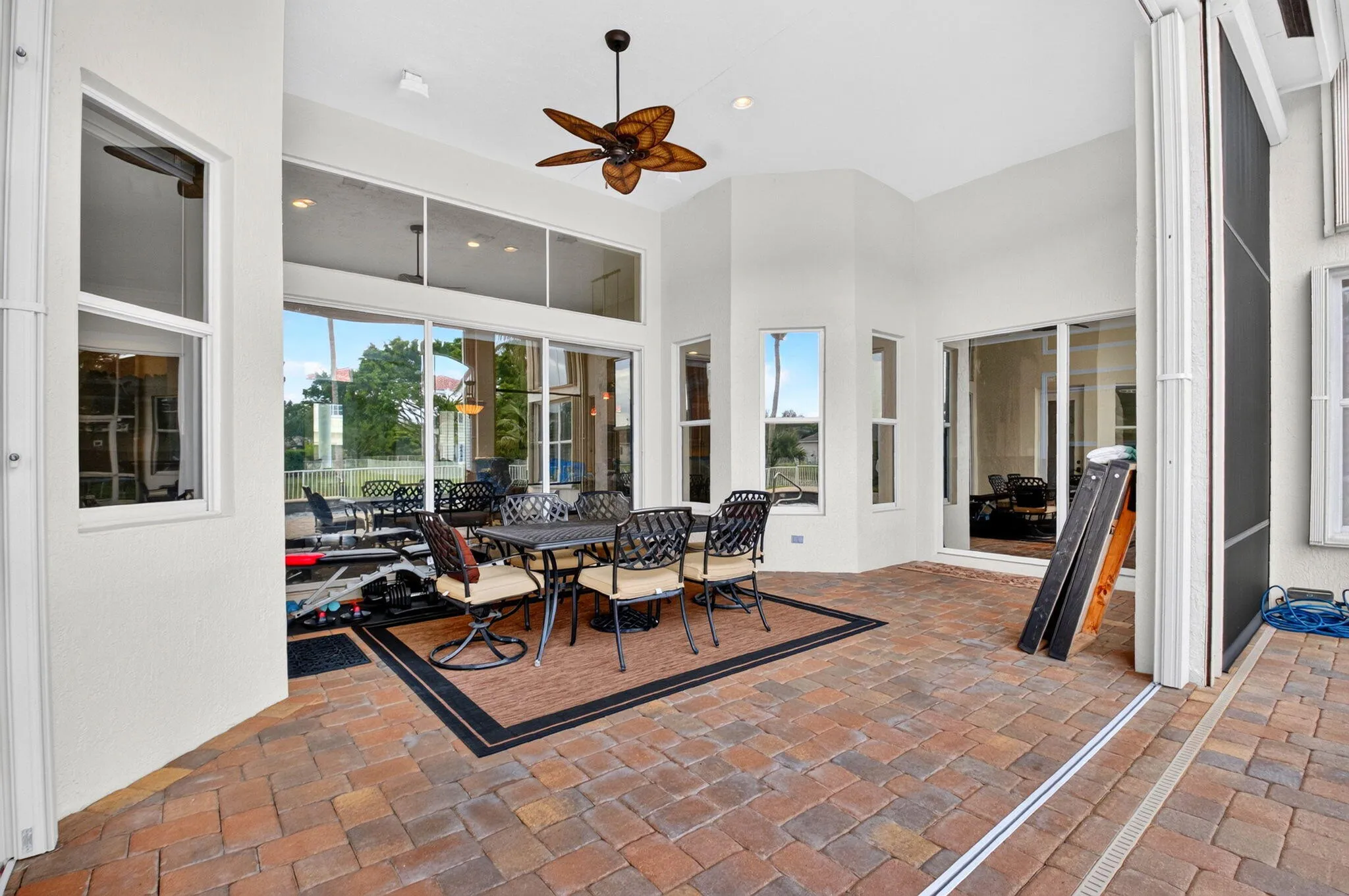 Spacious outdoor living area with brick paver flooring and an overhead ceiling fan
