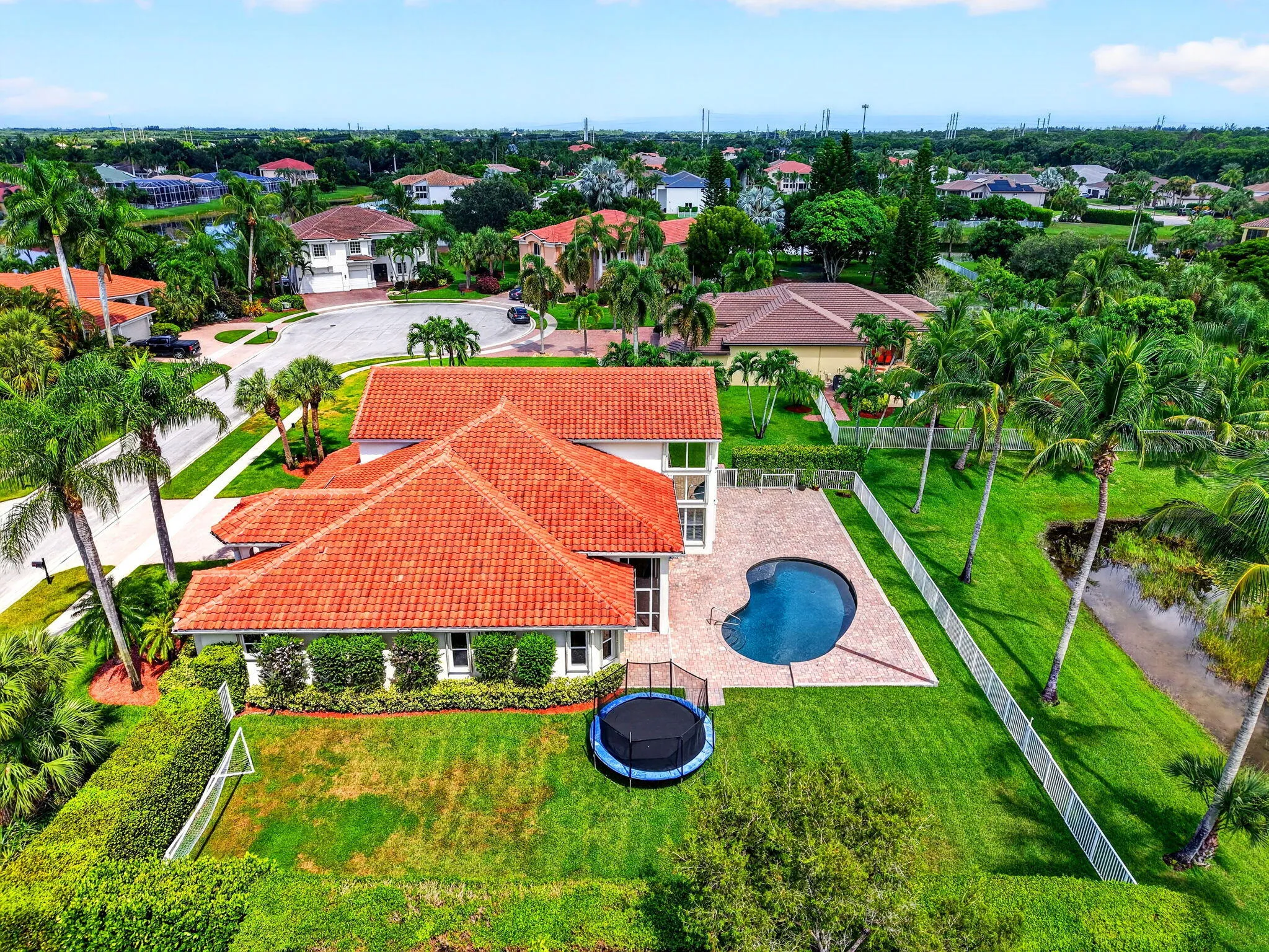 Tile roof residence with a kidney-shaped swimming pool, paved pool deck, and lush landscaping