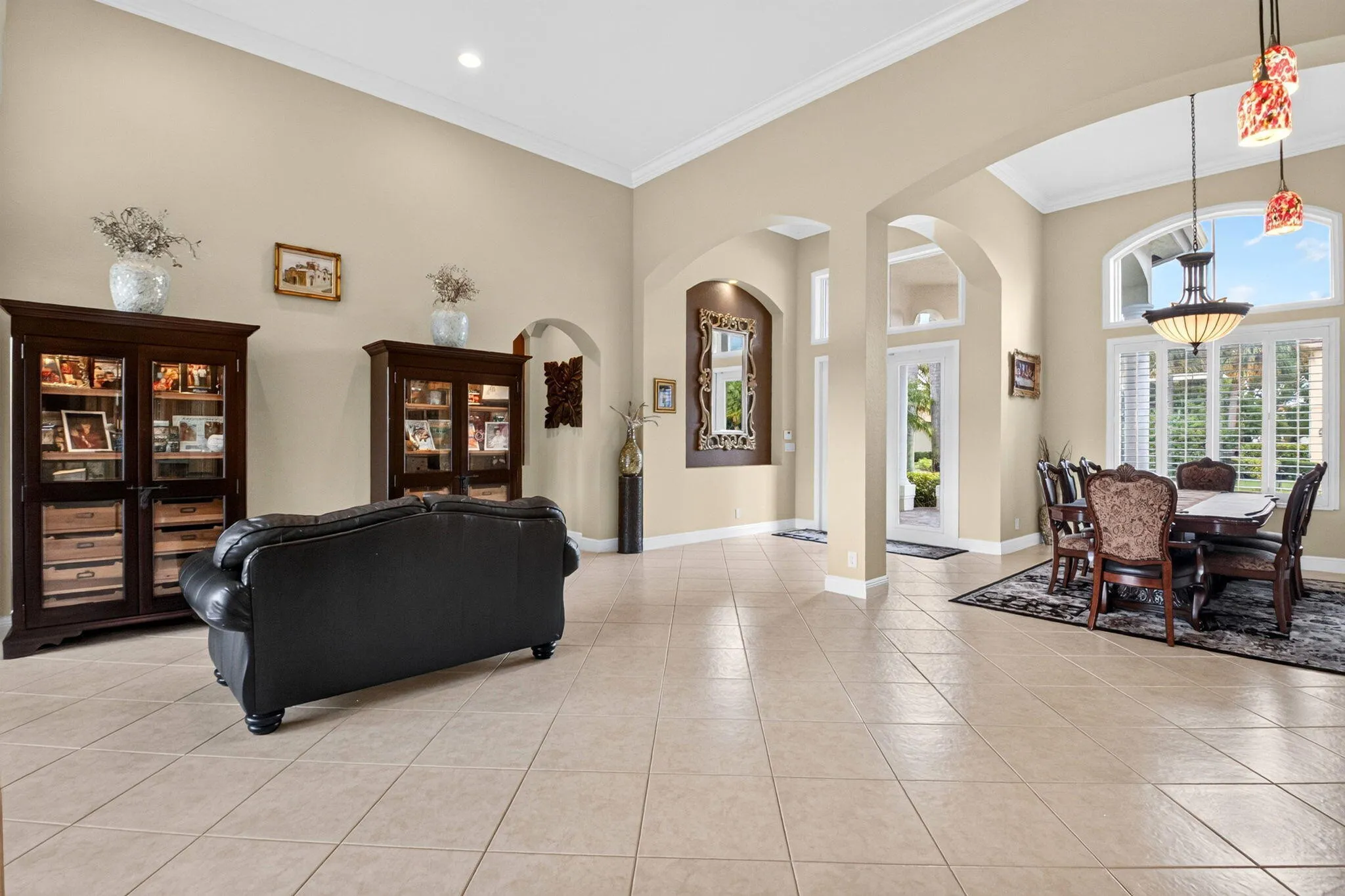 Arched doorways with crown molding, high ceilings, large windows with plantation shutters, and light-colored tile flooring