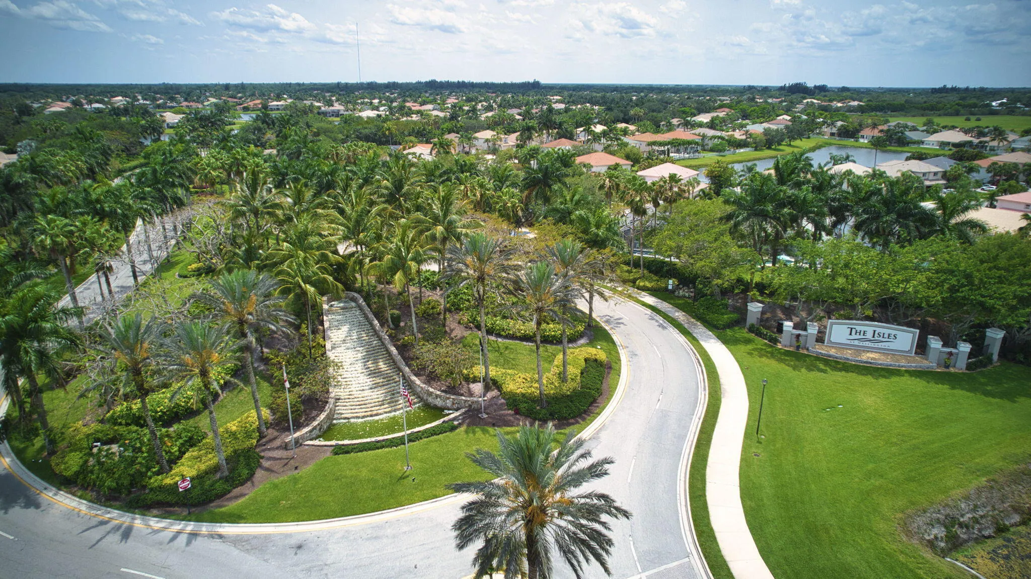 Gated entry with stone columns and integrated signage, surrounded by mature palm trees and lush landscaping