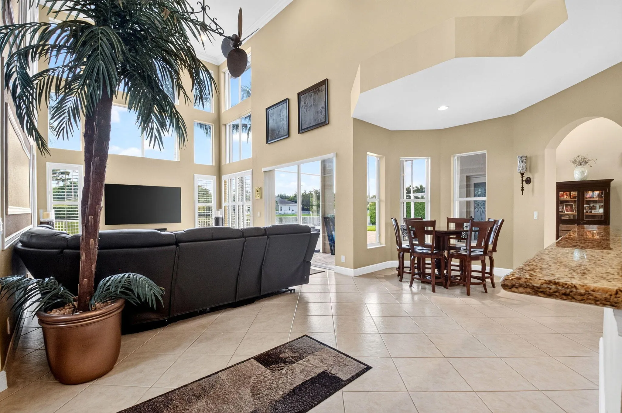 Vaulted ceiling with a ceiling fan, wall of windows with plantation shutters, tile flooring, built-in kitchen island with stone countertop, and arched entryway