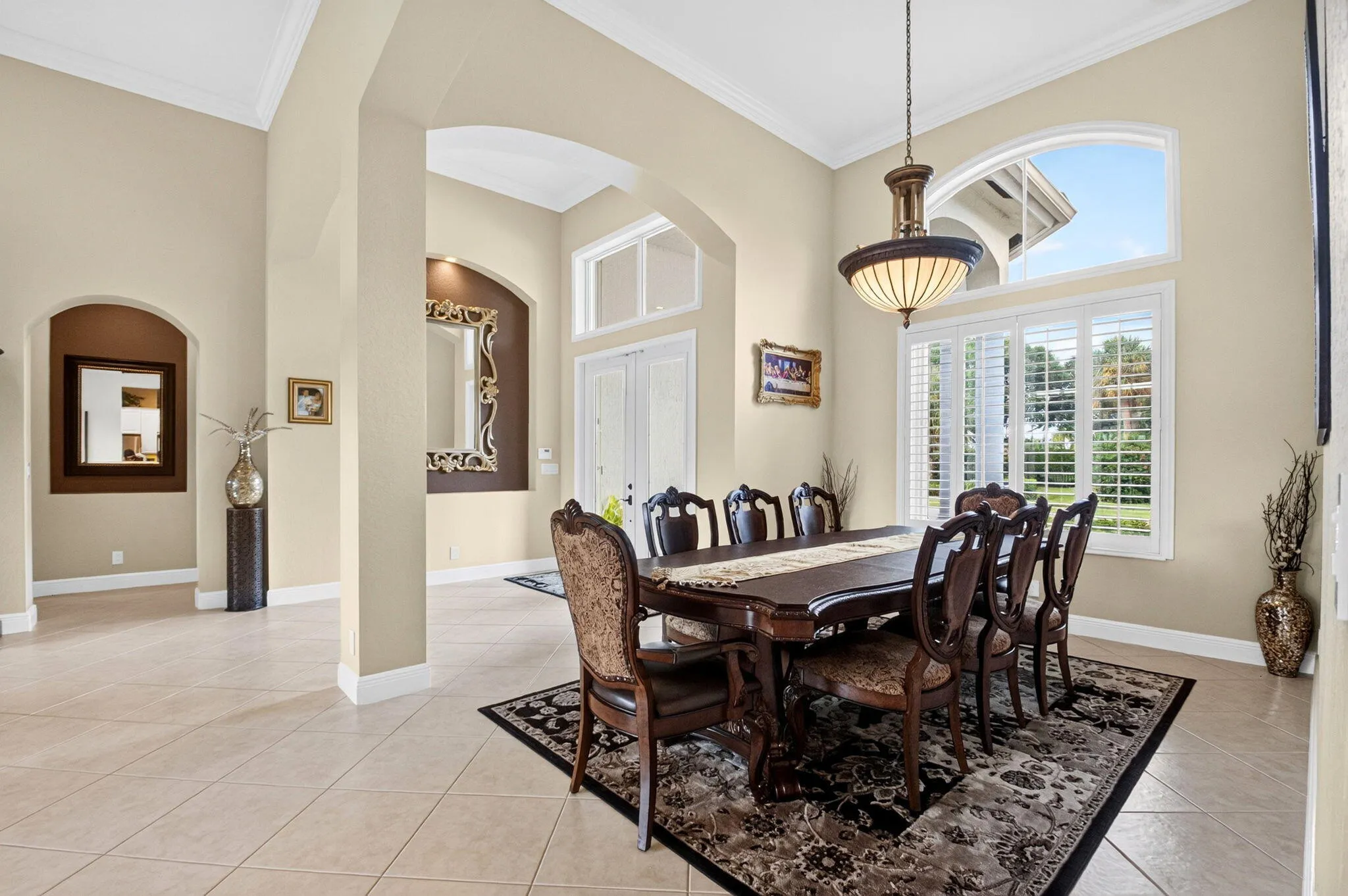 High ceilings with crown molding, arched entryways, plantation shutters, transom windows, and tile flooring