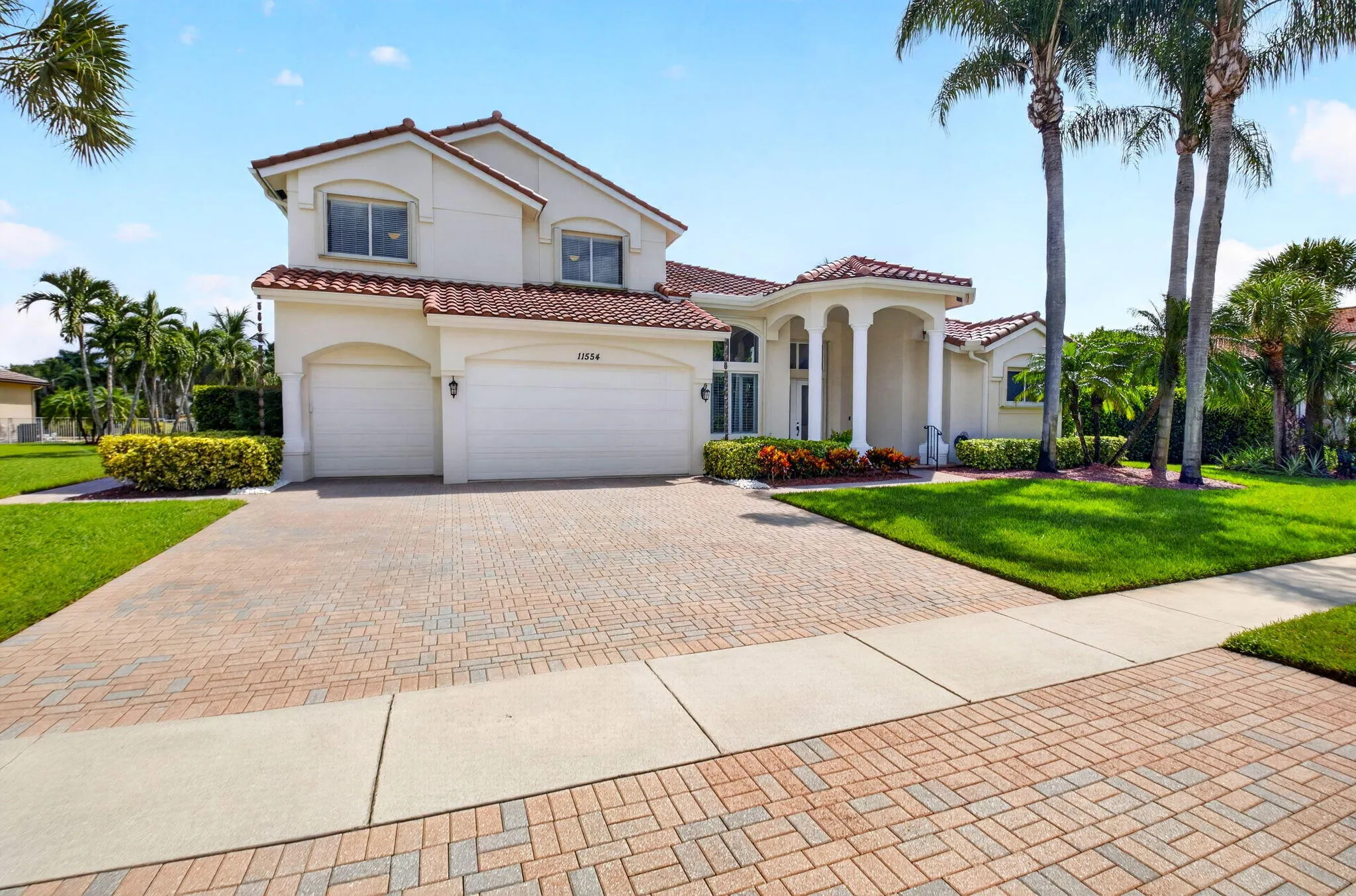 Stucco exterior with a tile roof, three-car garage, a columned portico, mature palm trees, and a paver driveway