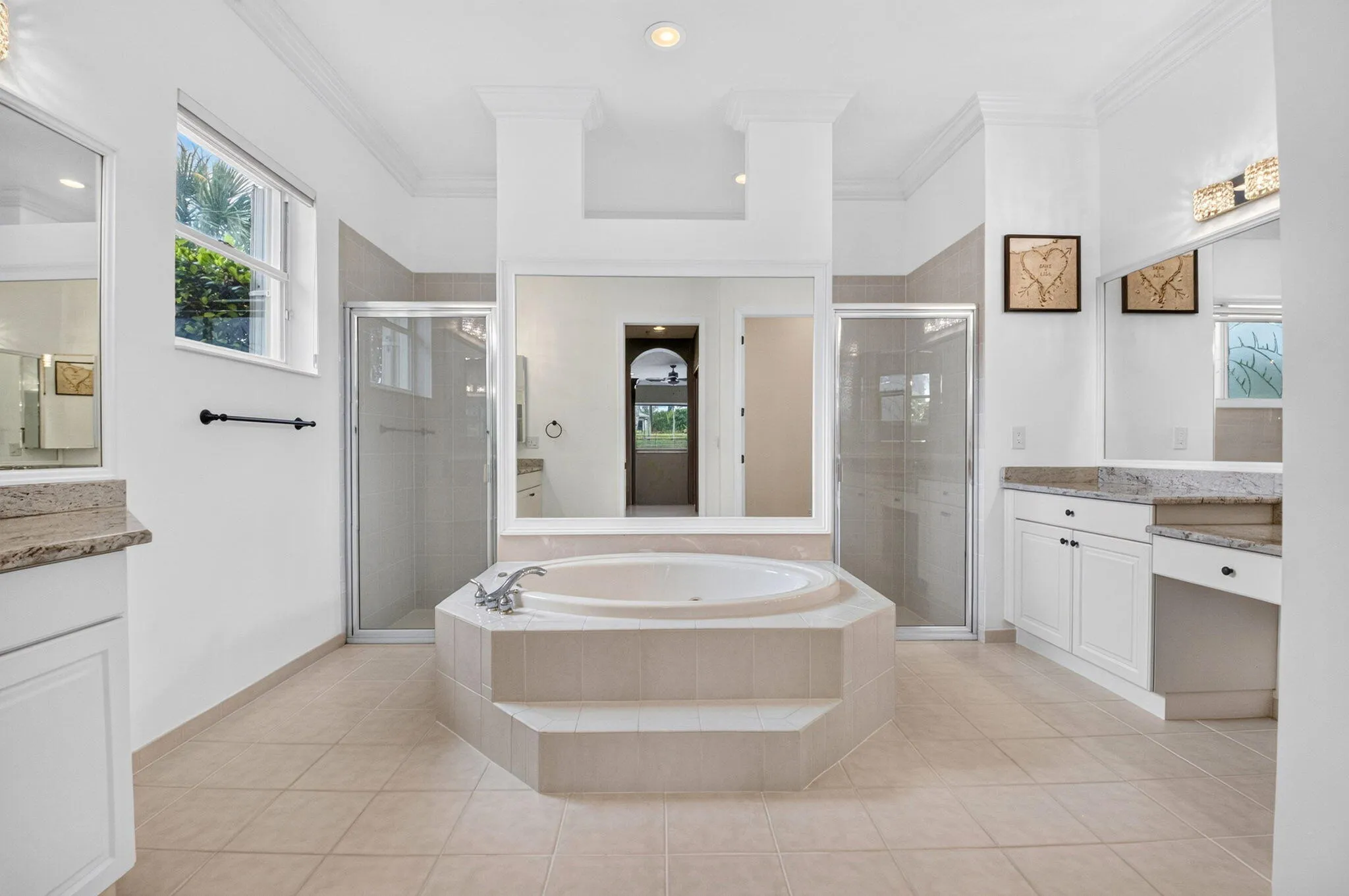 Expansive bathroom featuring a built-in jetted tub, dual walk-in showers with glass enclosures, twin vanity stations with integrated sinks and storage, and large windows