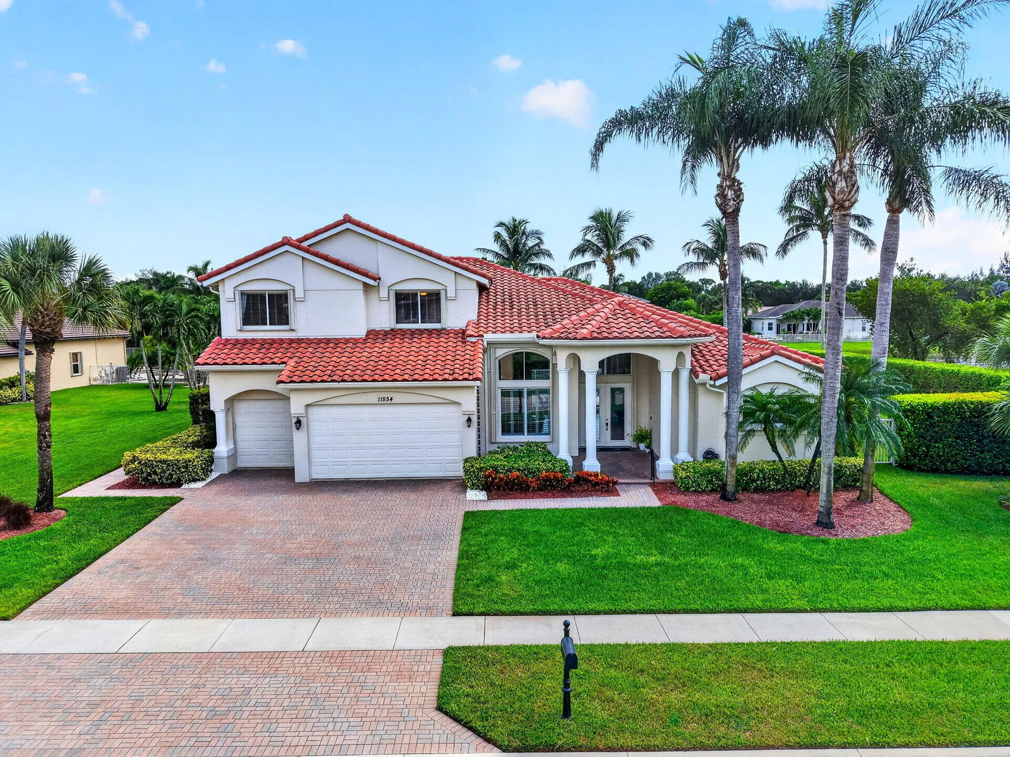 Mediterranean-style architecture with a red barrel tile roof, two-car garage, brick paver driveway, and mature landscaping