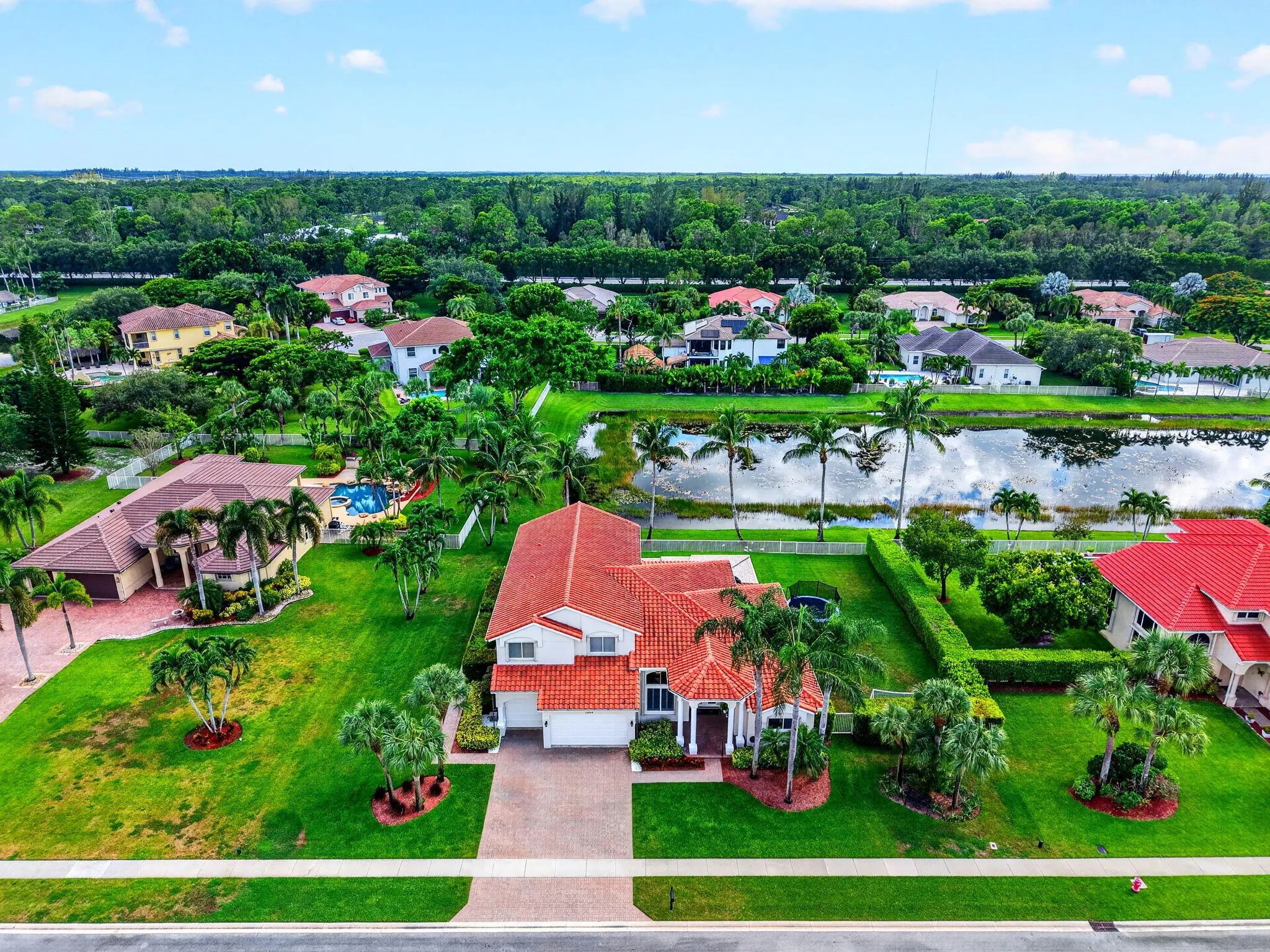 Red tile roof, mature landscaping, paved driveway, two-car garage, and stucco exterior