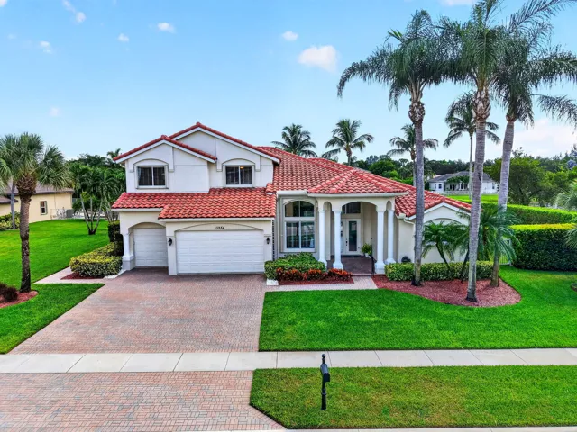 Mediterranean-style architecture with a red barrel tile roof, two-car garage, brick paver driveway, and mature landscaping
