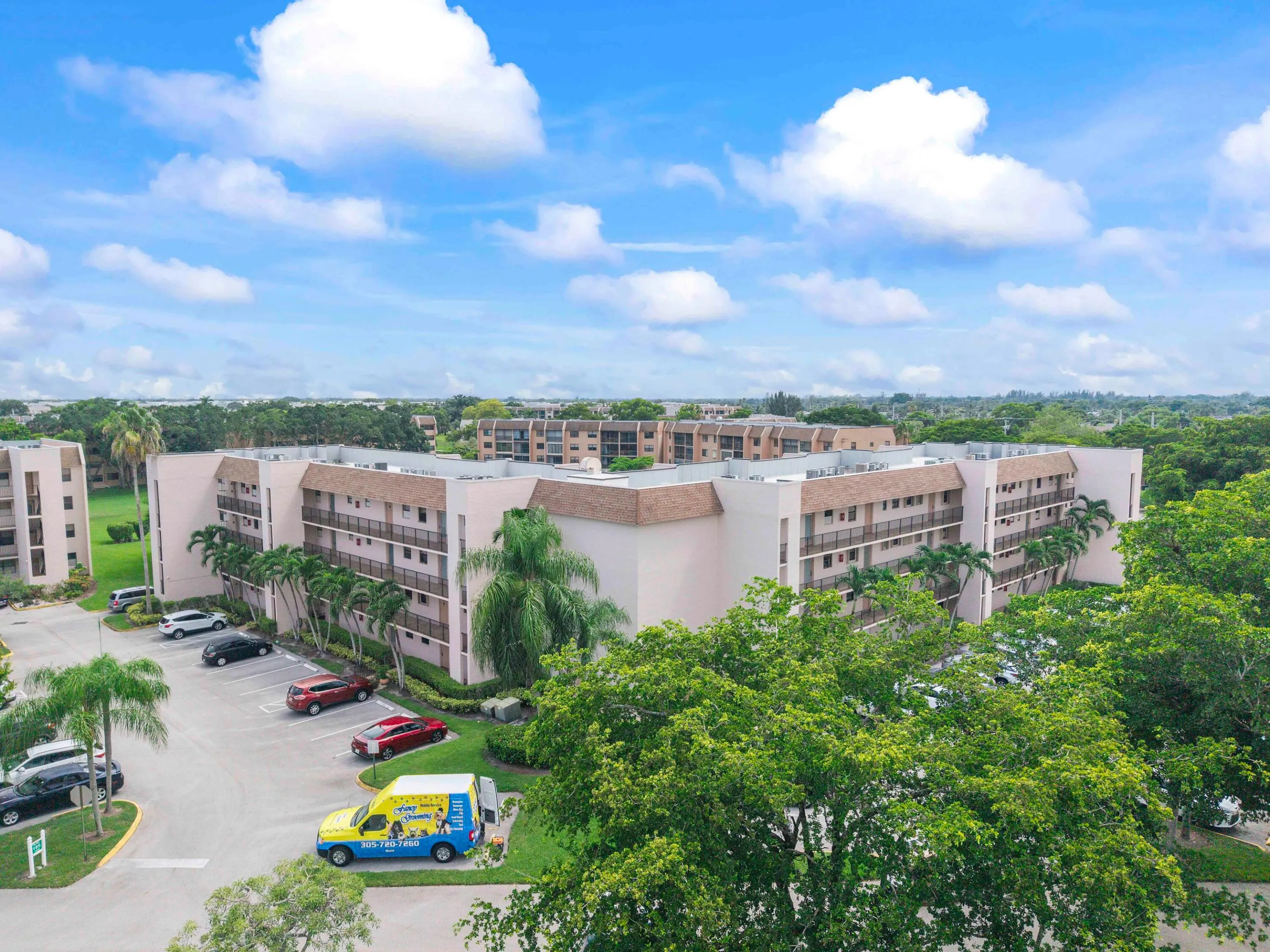 Multi-story building featuring multiple private balconies, a paved parking area, and mature landscaping