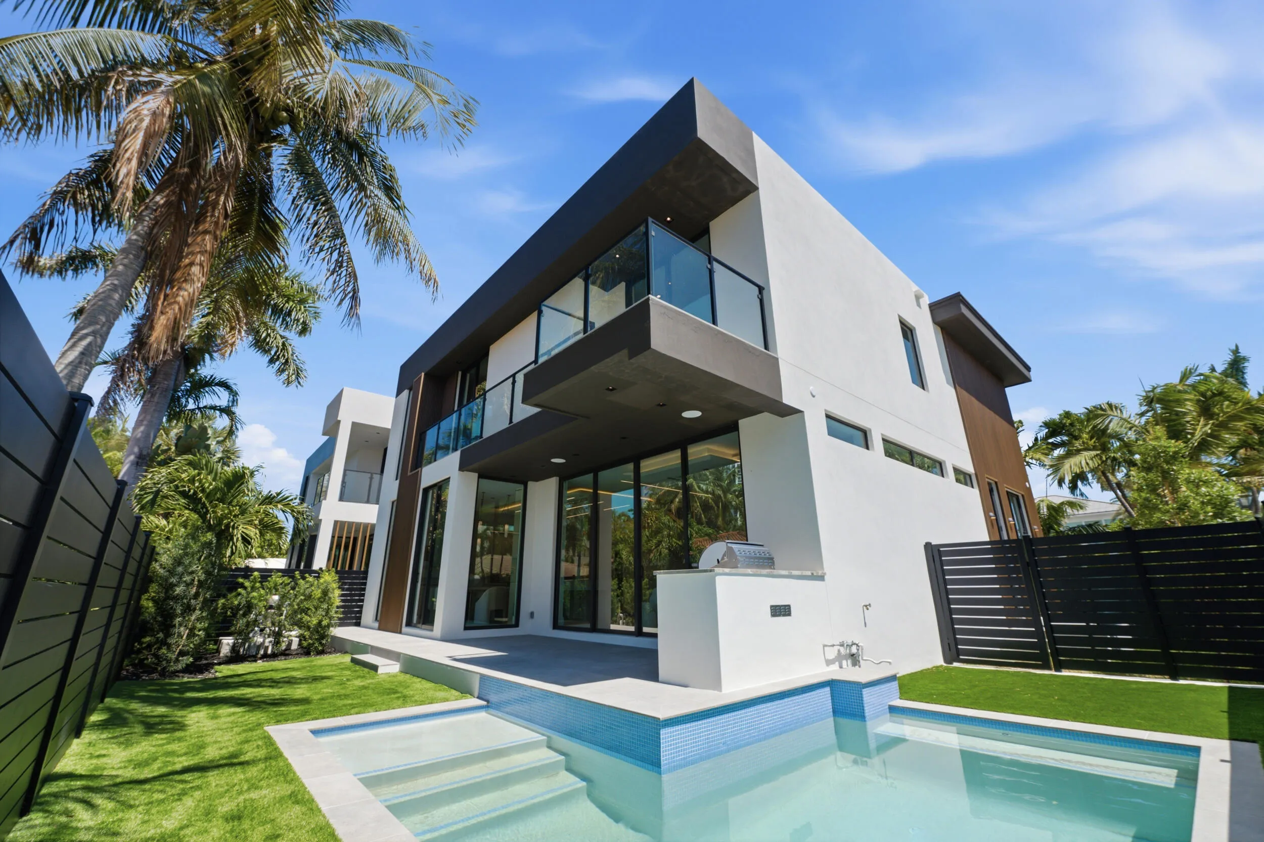 Contemporary two-story exterior with a flat roofline, an integrated garage, a paved driveway, a second-story balcony with a glass railing, and a ground-floor entry with a dark door