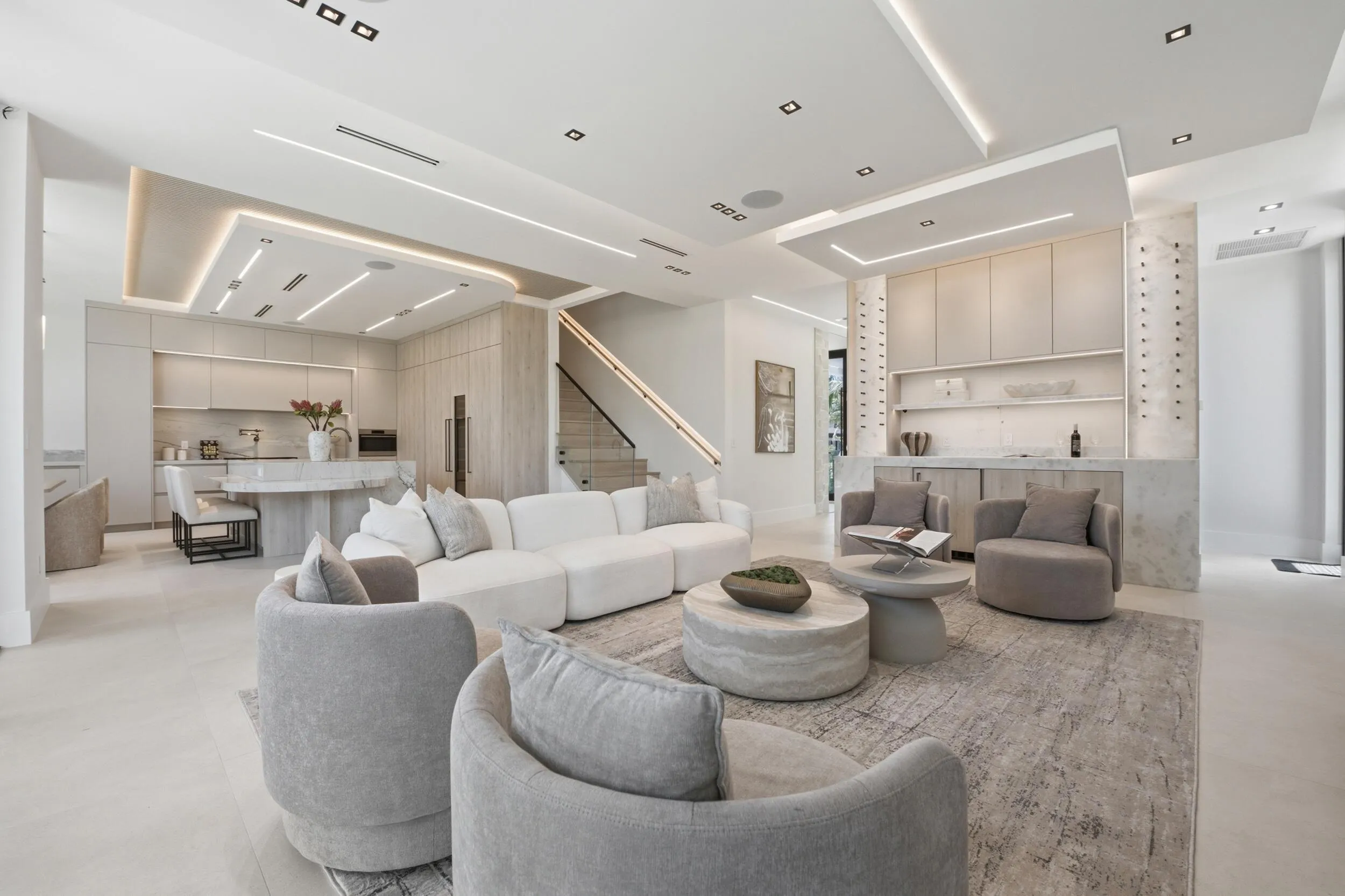 Open-concept living space featuring a built-in wet bar, gourmet kitchen with island, and a modern staircase with a black handrail