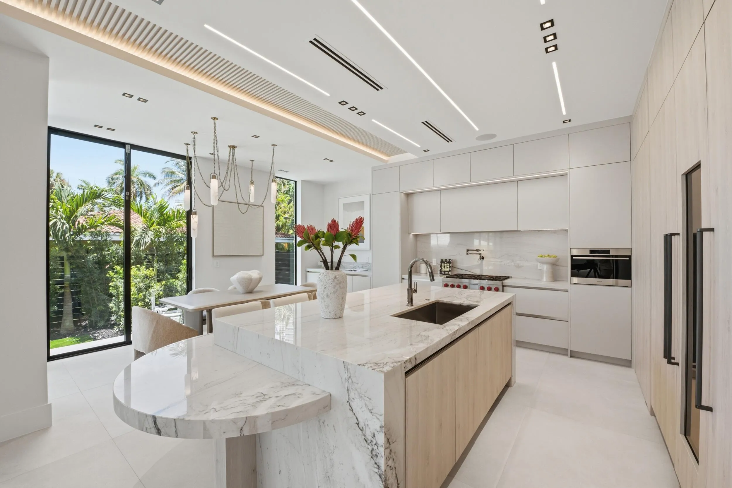 Gourmet kitchen featuring a waterfall island, integrated appliances, white cabinetry, and extensive full-height windows