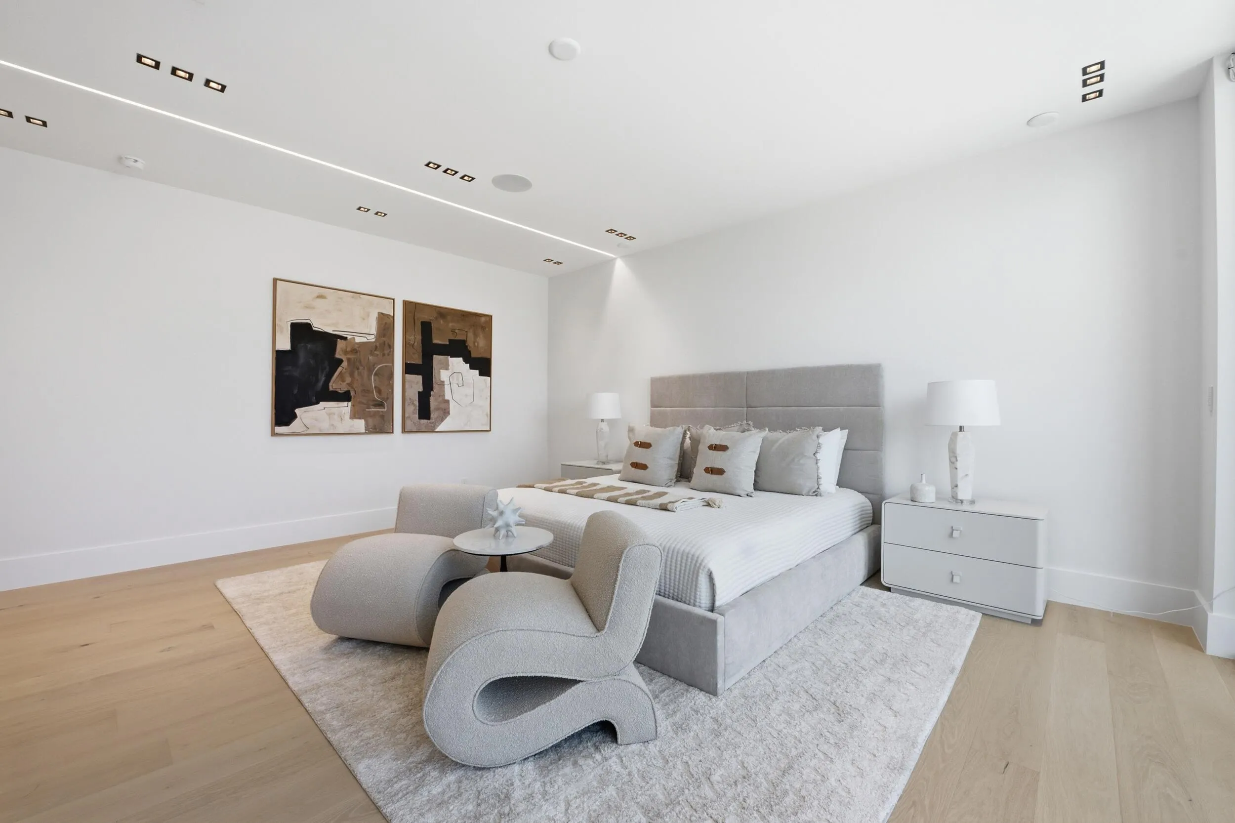 Recessed ceiling lighting, linear ceiling lighting, light wood-finish flooring, white walls, and a built-in upholstered headboard