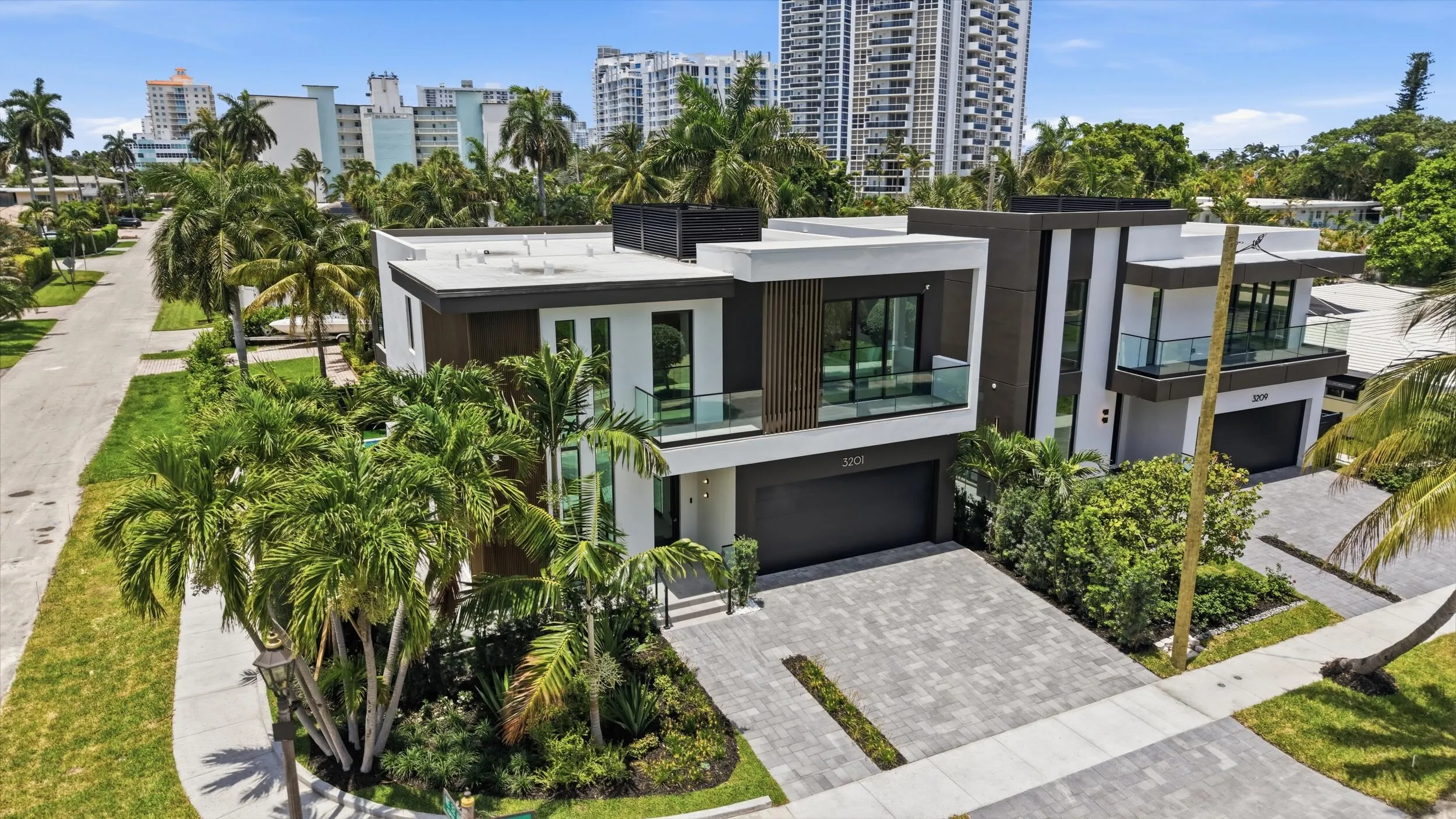 Contemporary architecture featuring a white and dark facade, multiple balconies with glass railings, large windows, an integrated two-car garage, and a paver driveway
