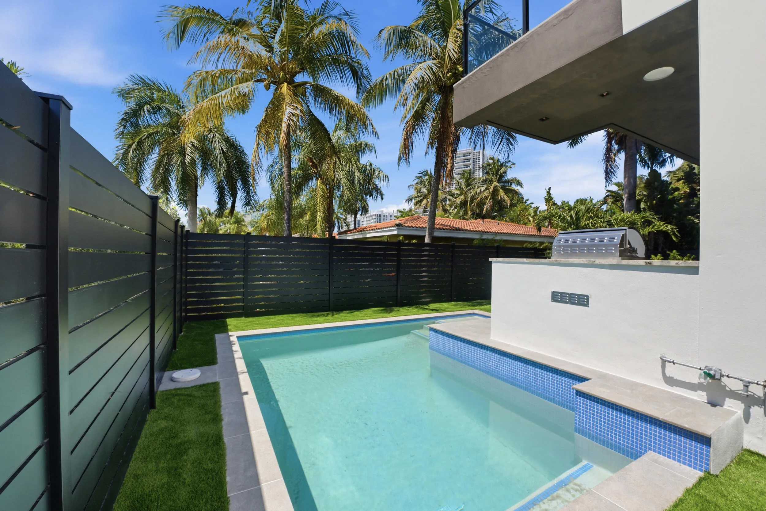 Outdoor swimming pool with blue mosaic tile accents, integrated built-in grill, and artificial turf surrounds