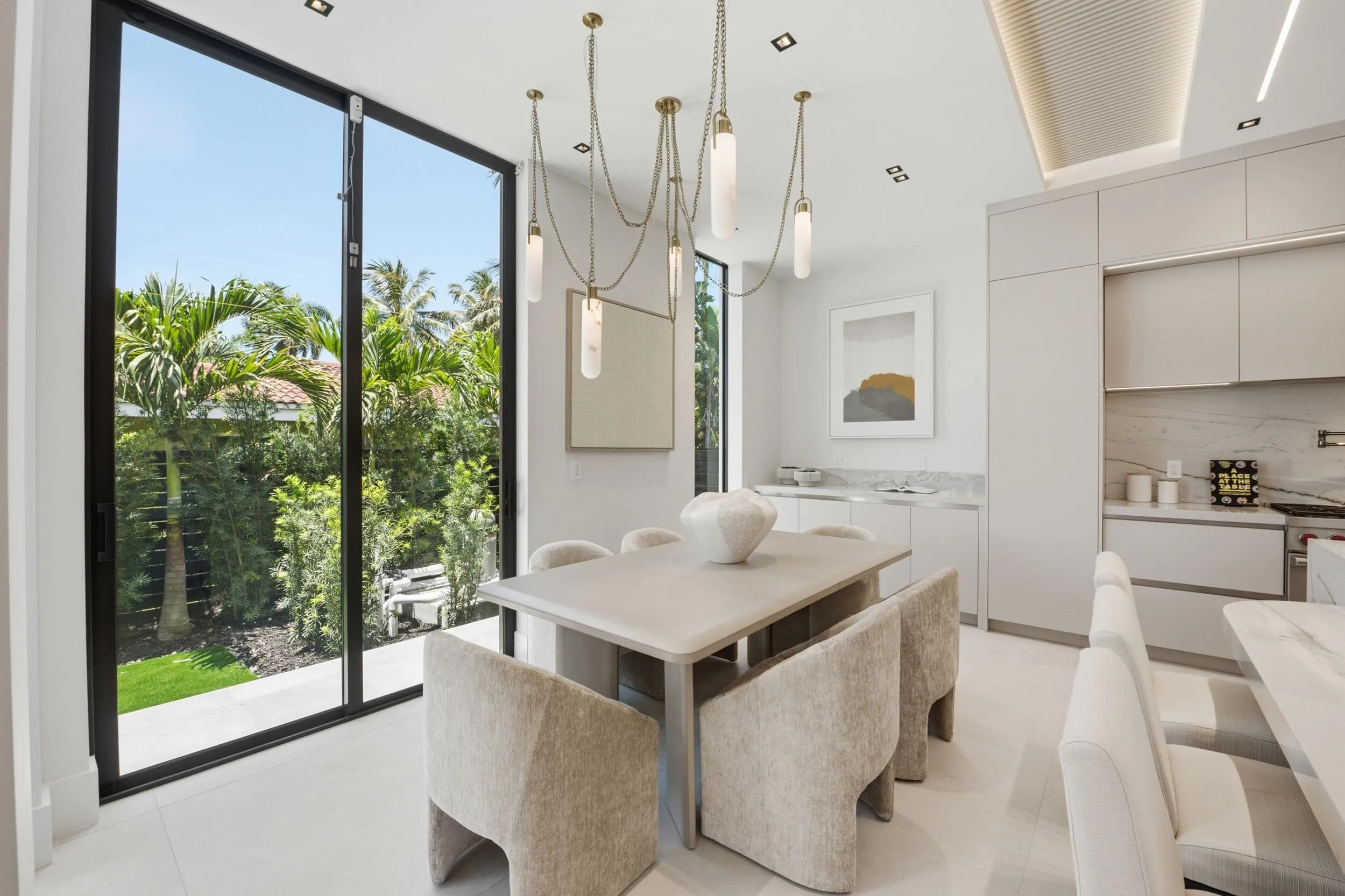 Integrated kitchen and dining area featuring floor-to-ceiling glass doors, recessed lighting, a multi-pendant light fixture, and built-in cabinetry with stone countertops