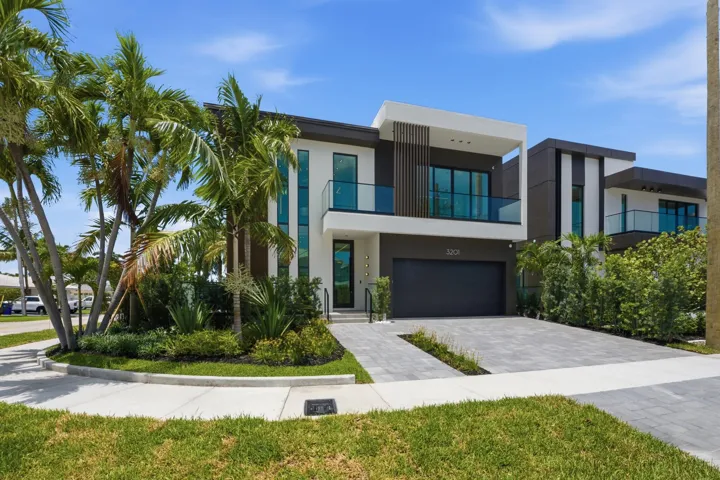 Modern two-story exterior with a flat roofline, glass panel balconies, a paver driveway, and an integrated garage