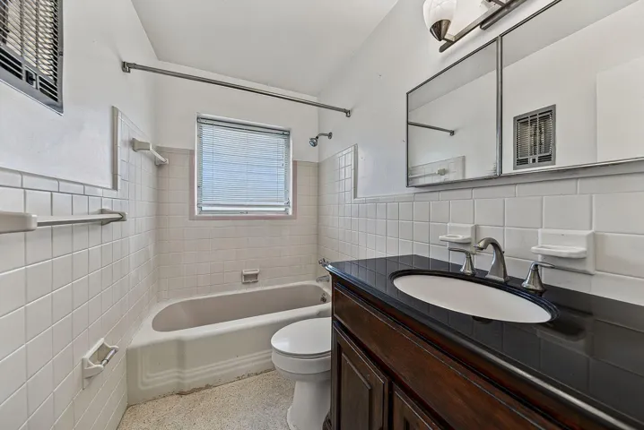 Full bathroom with tub-and-shower combination, tiled walls and a dark countertop vanity.