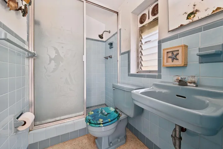 Full bathroom with a tiled shower, pedestal sink and window providing natural light.