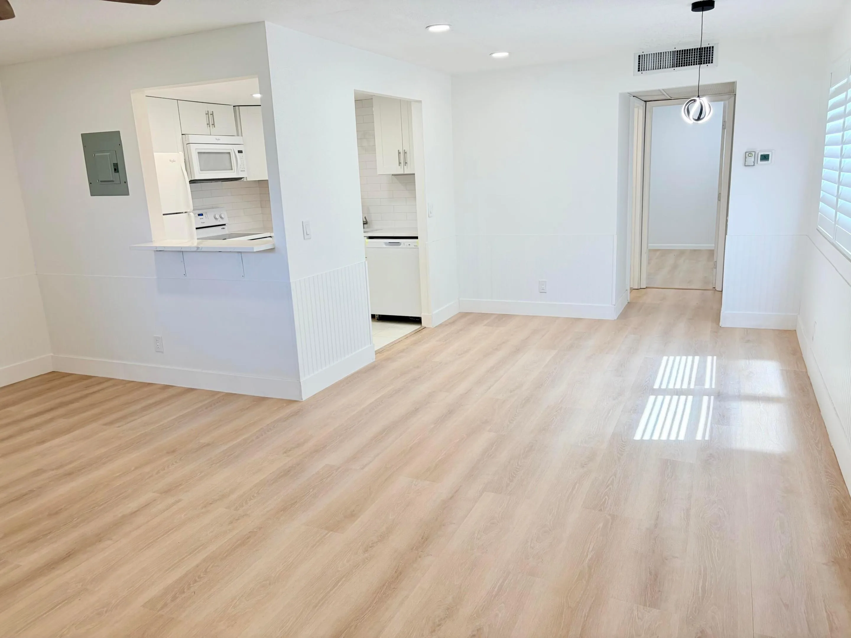 Open-concept living area with wood-finish flooring, white walls, recessed lighting, and a modern pendant light fixture
