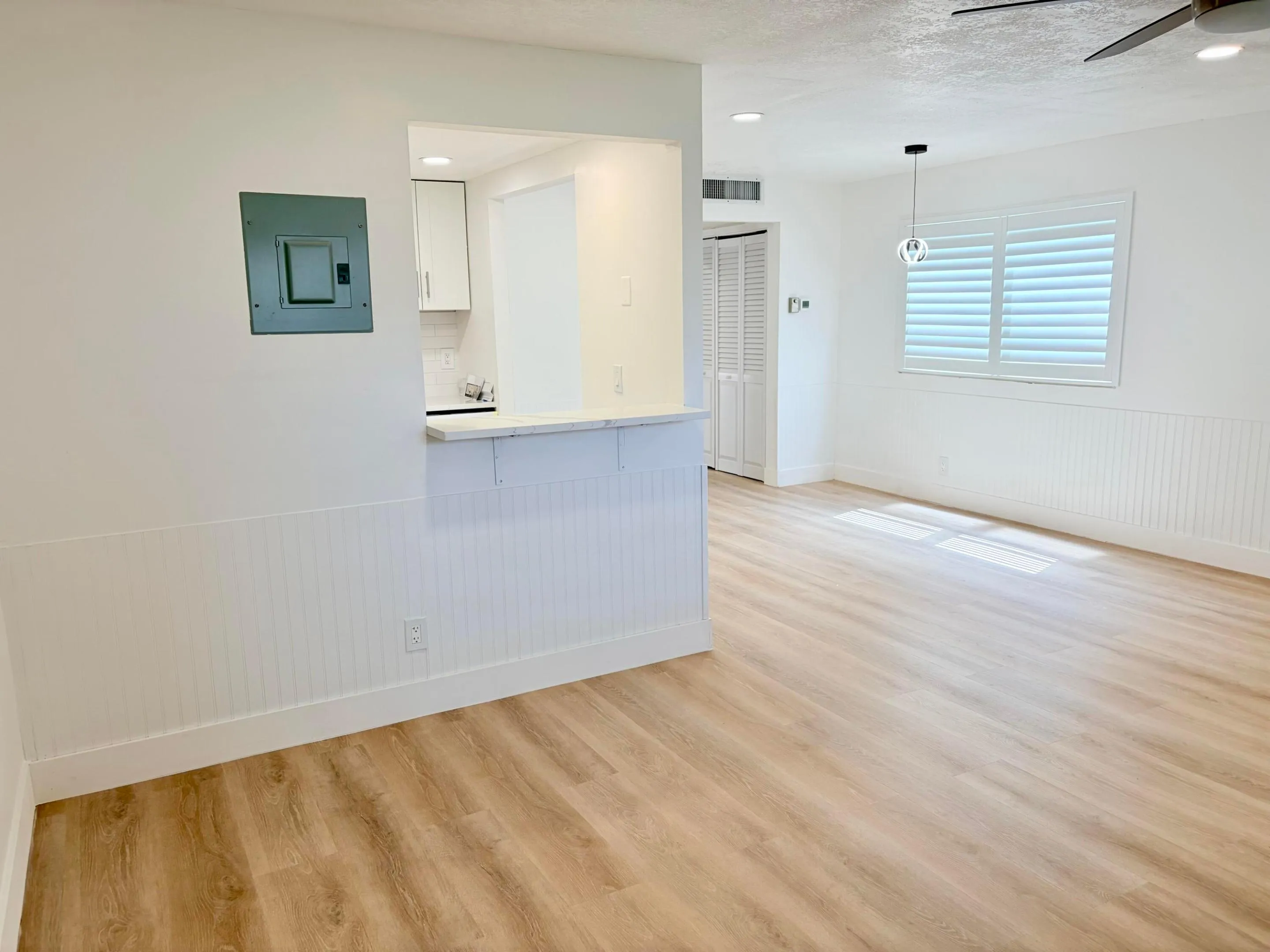 Wood-finish flooring throughout, white beadboard wainscoting, and a kitchen pass-through with a breakfast bar