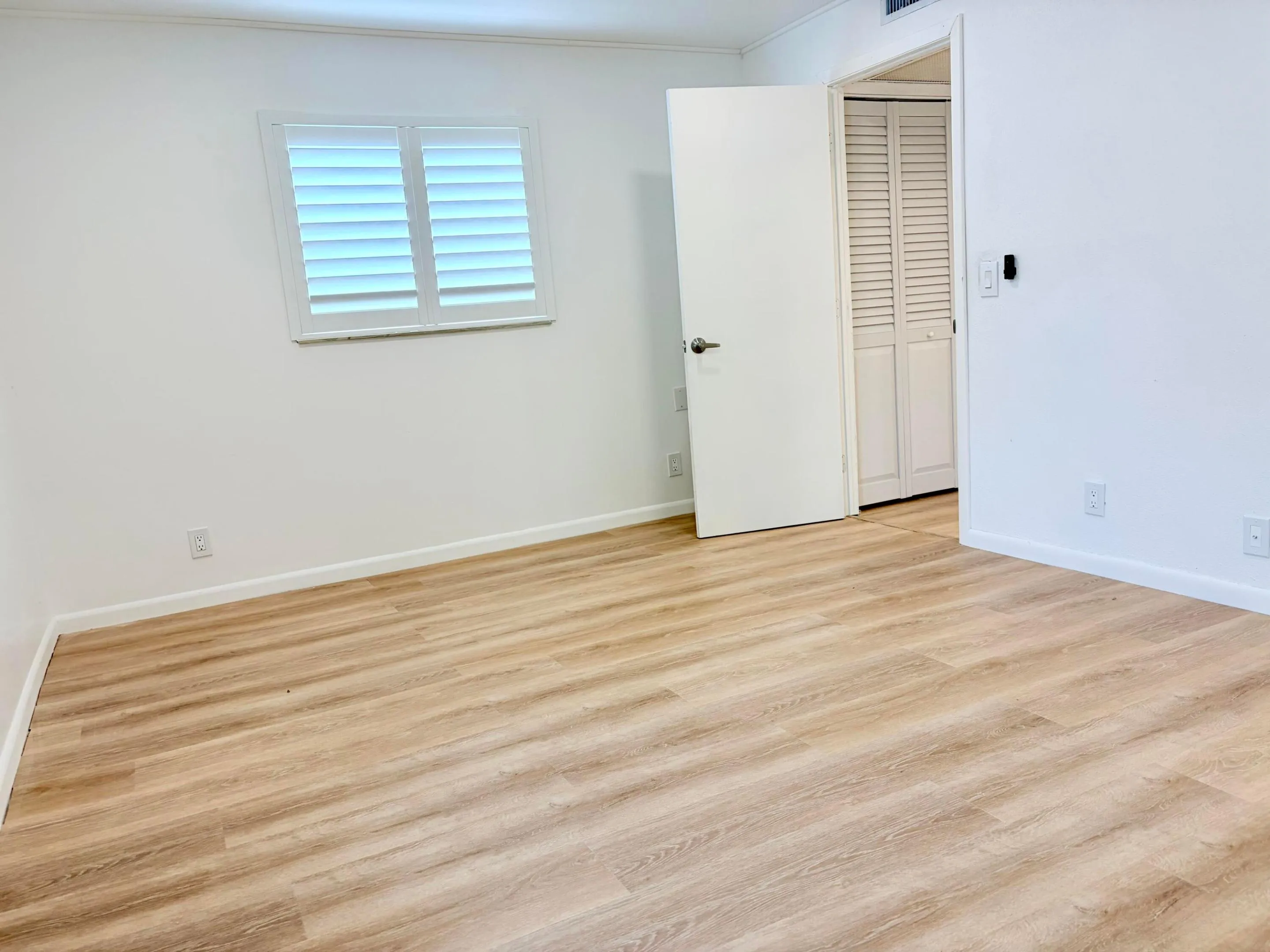 Wood-finish flooring with white walls and a window featuring plantation shutters