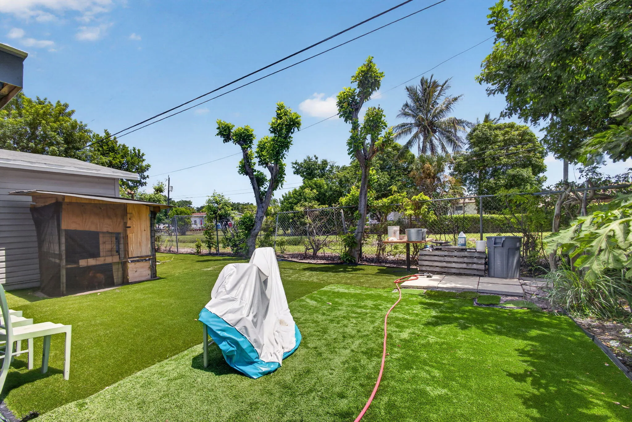 Expansive backyard featuring artificial turf, mature trees, a chain-link fence, and a wooden shed