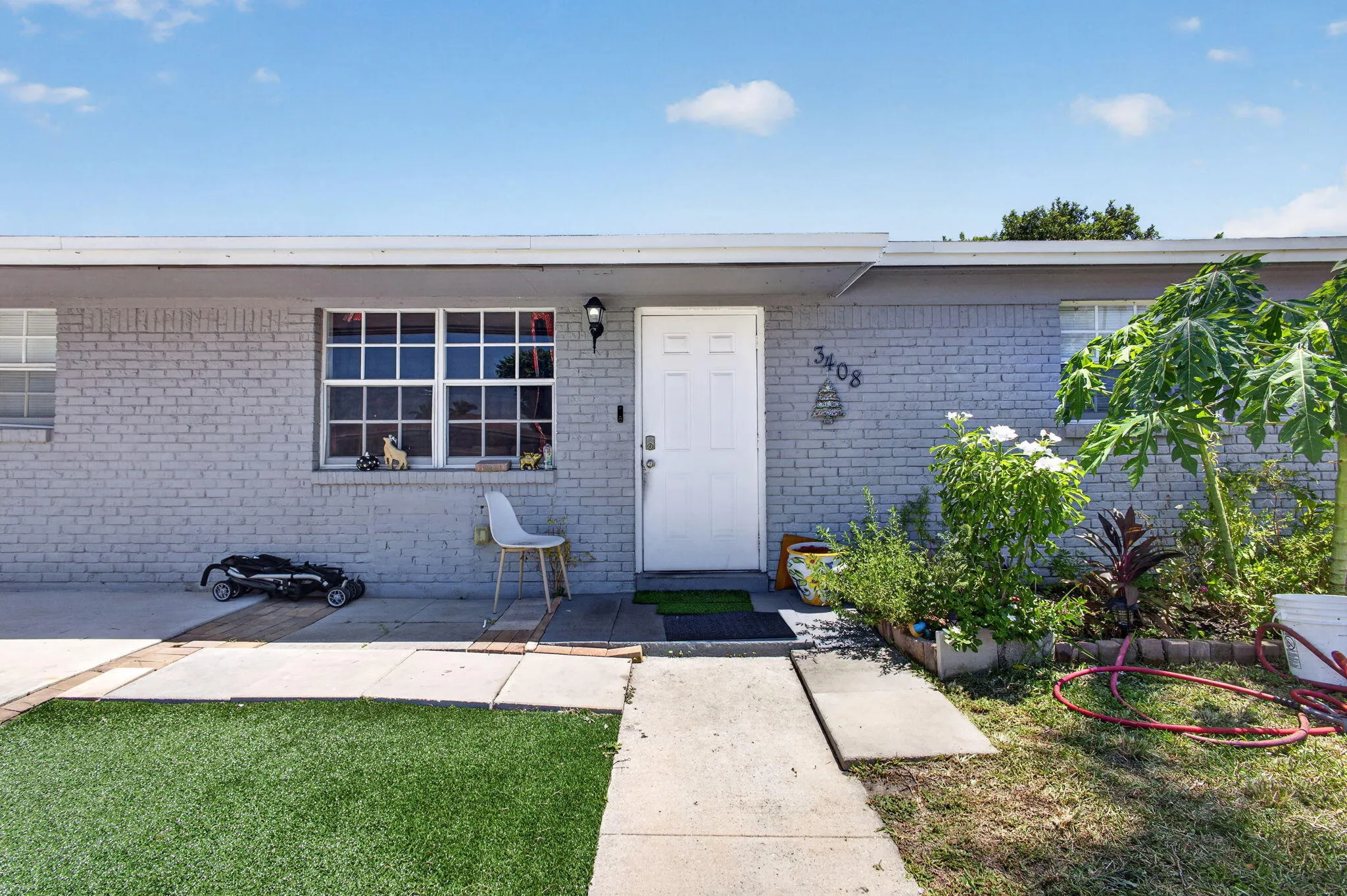 Gray brick exterior with white trim, a white entry door, and a front window with gridded panes