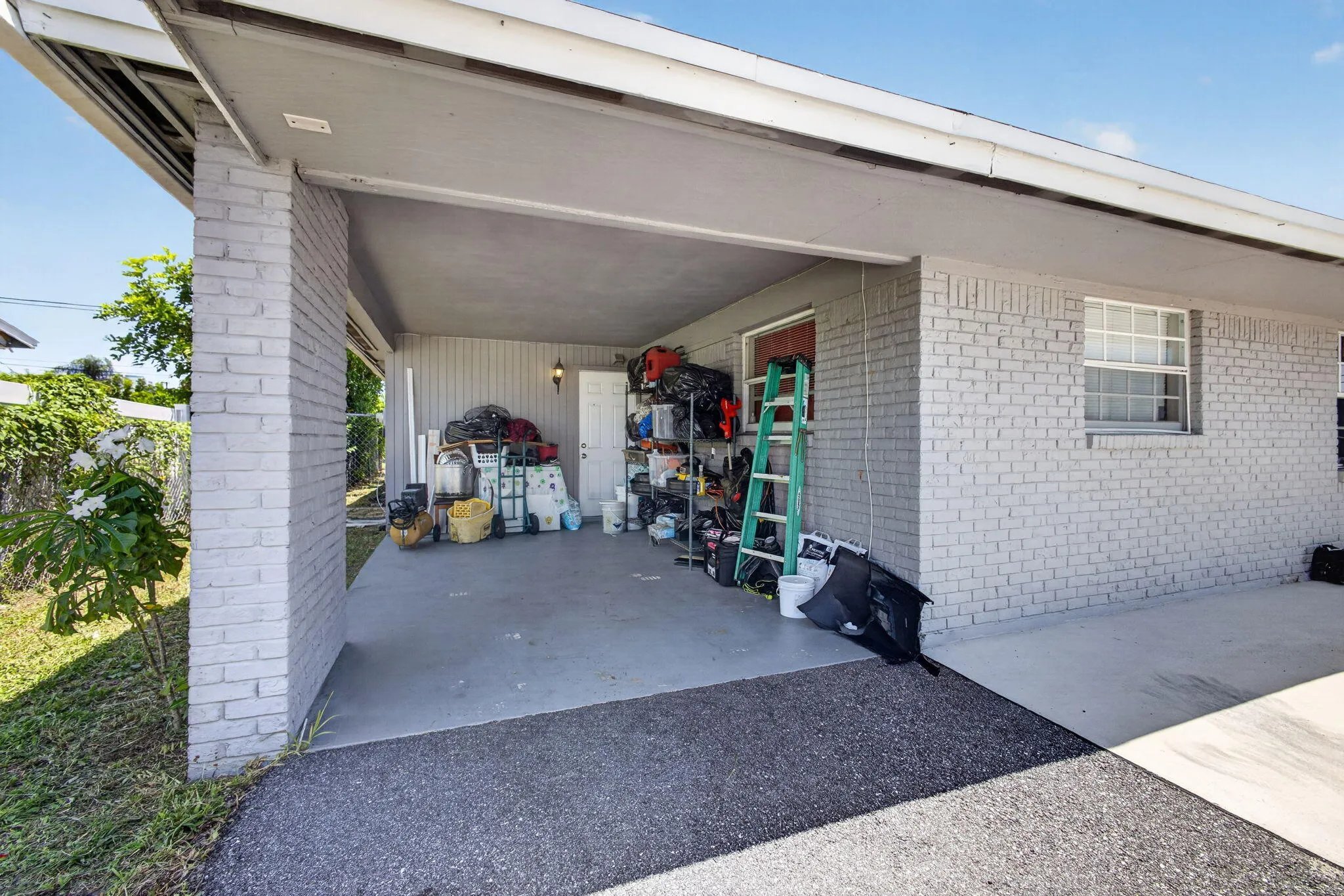 Carport with an asphalt driveway, concrete pad, painted brick exterior, and a white-framed window