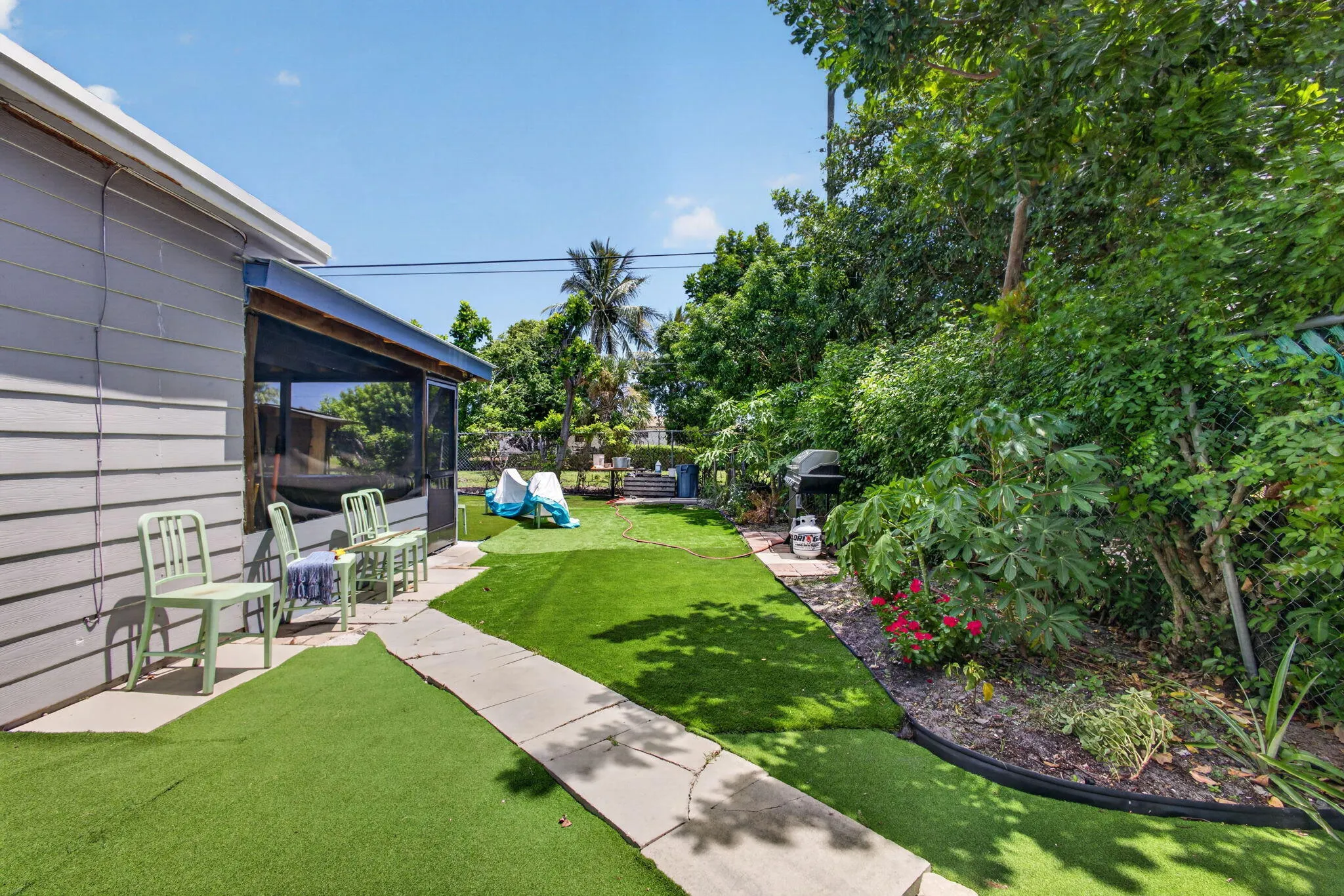 Expansive backyard featuring a screened porch, artificial turf, concrete pathway, and mature landscaping