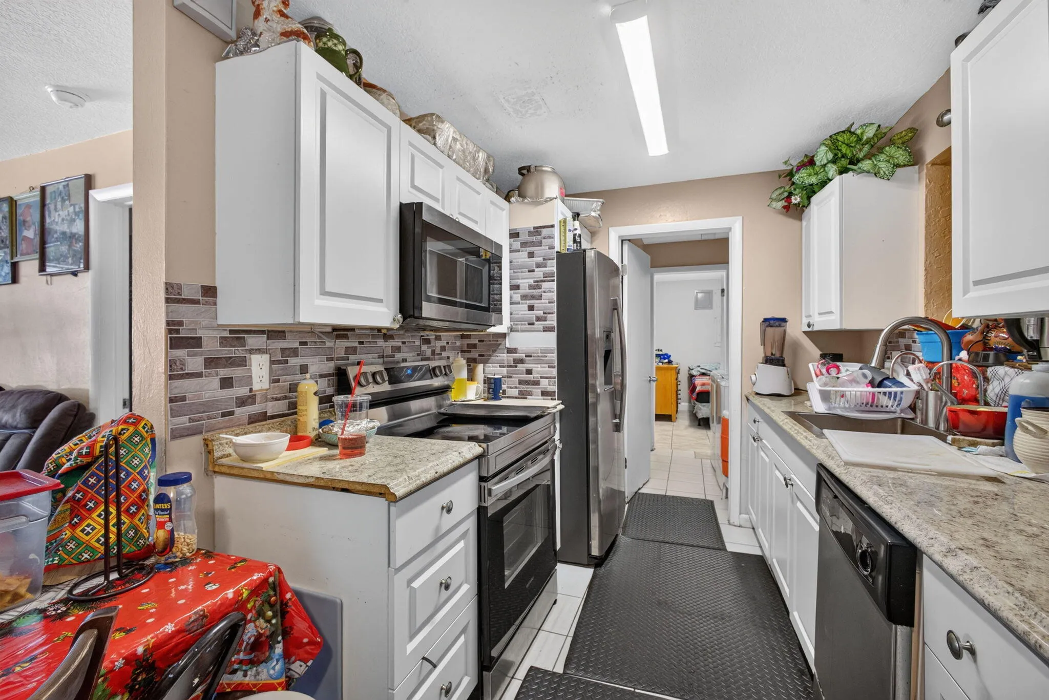 White cabinetry, stone-finish countertops, subway tile backsplash, stainless steel appliances, and tile flooring