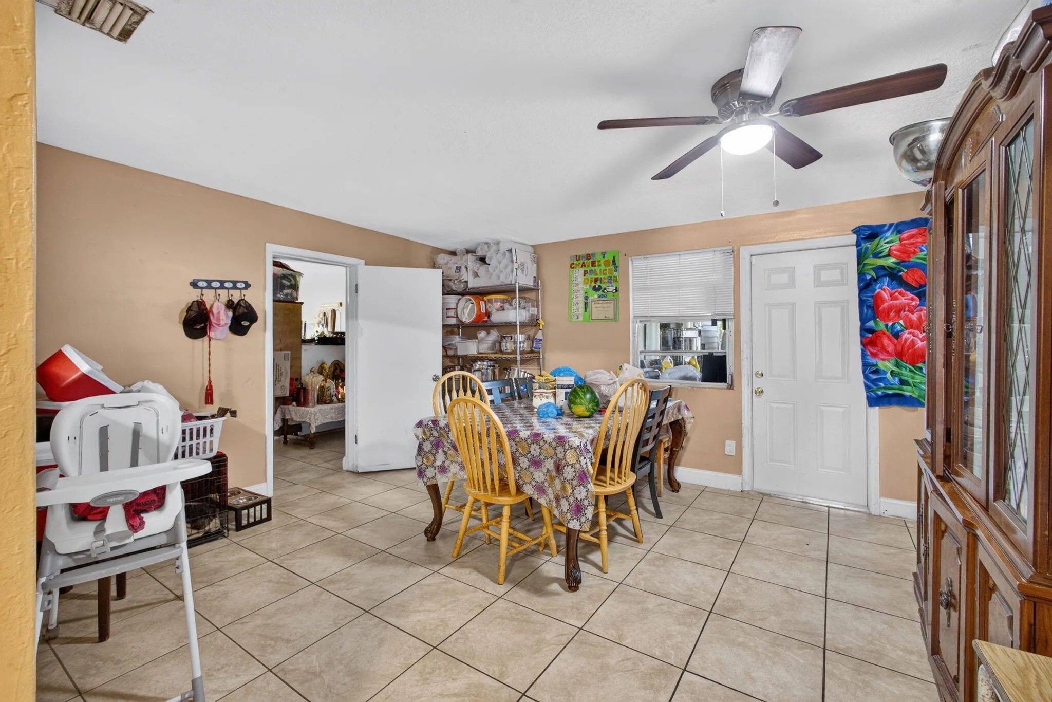 Tile flooring, ceiling fan with integrated lighting, window with blinds, white paneled door, built-in wooden display cabinet