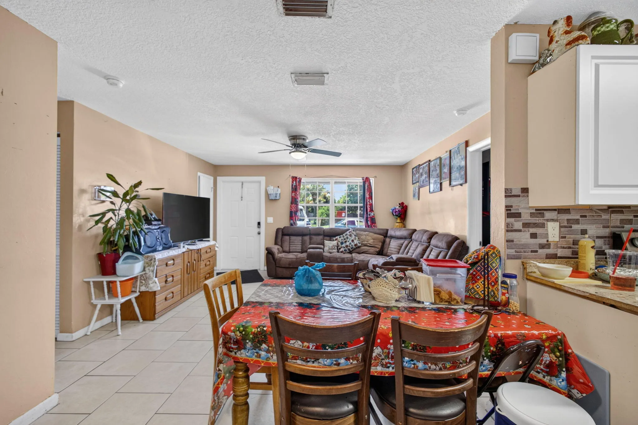 Open concept living and dining area featuring ceramic tile flooring, a ceiling fan, and a kitchen with white cabinetry and a mosaic tile backsplash