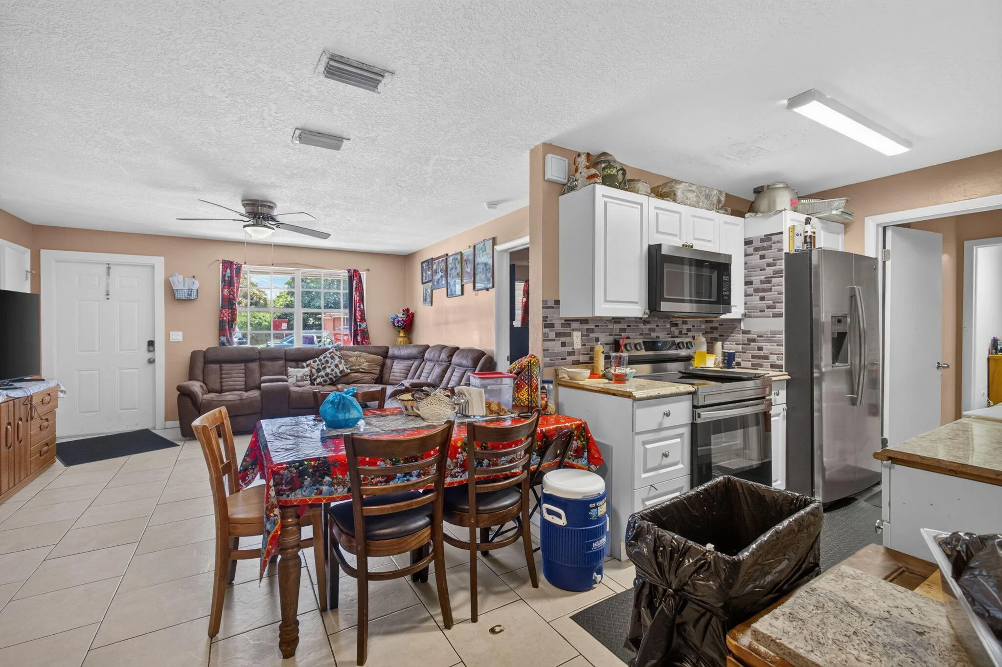 Combined kitchen and living space featuring tile flooring, white cabinetry, a tiled backsplash, and stainless steel appliances