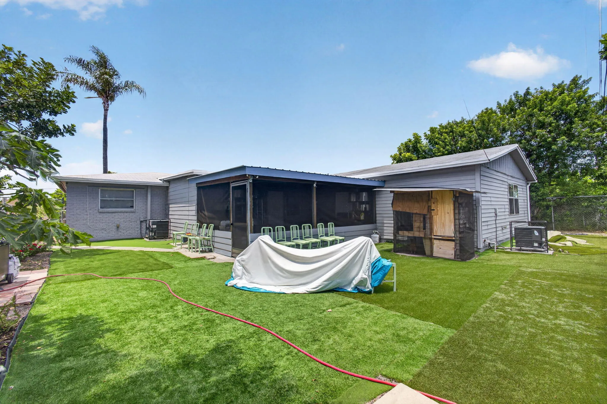 Expansive backyard featuring artificial turf, a screened-in patio, and a dedicated utility shed