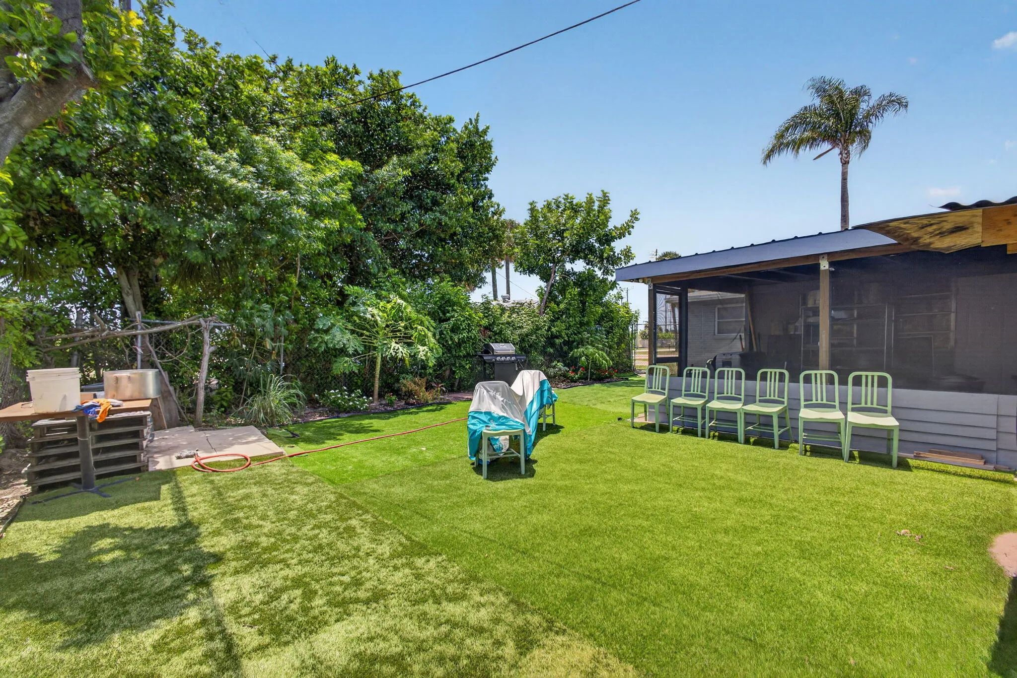 Expansive backyard featuring artificial turf, mature trees, and a screened-in porch with an overhead roof