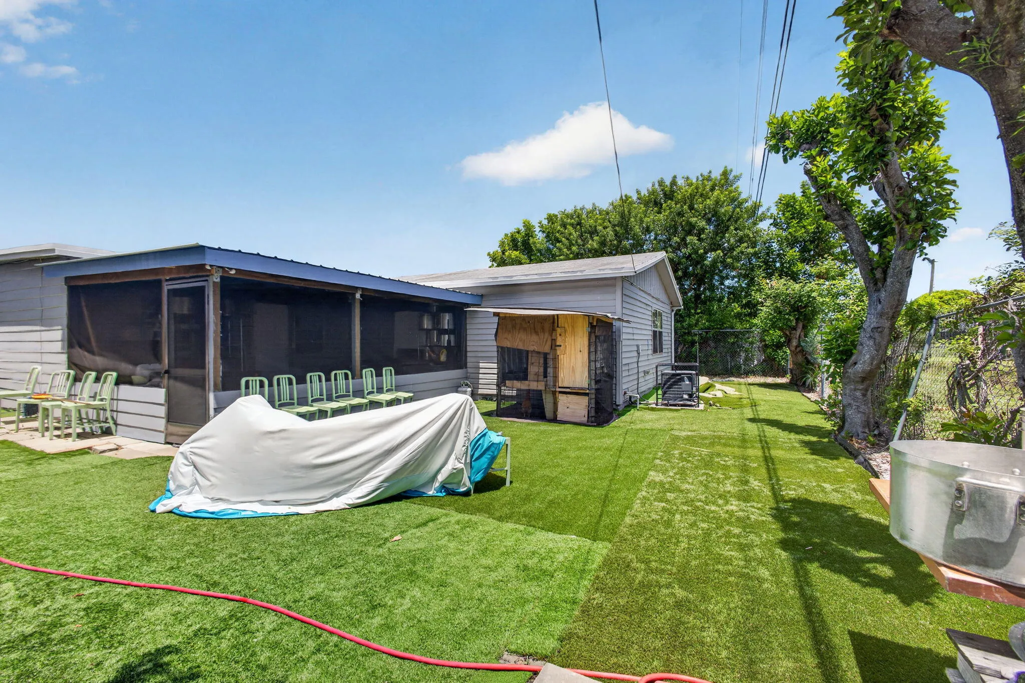 Expansive artificial turf backyard featuring a screened-in porch, mature trees, and a utility shed
