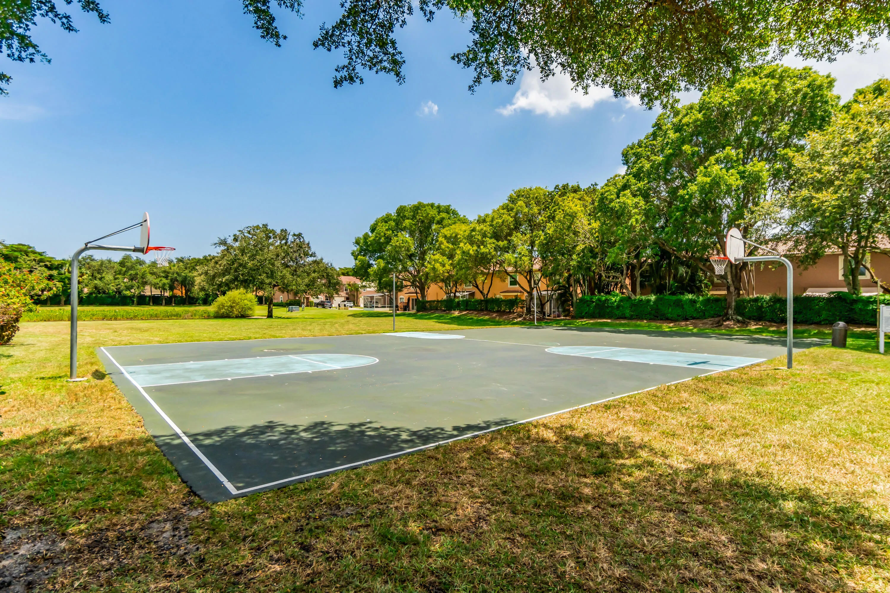 Outdoor basketball court with two hoops, surrounded by green space and mature trees