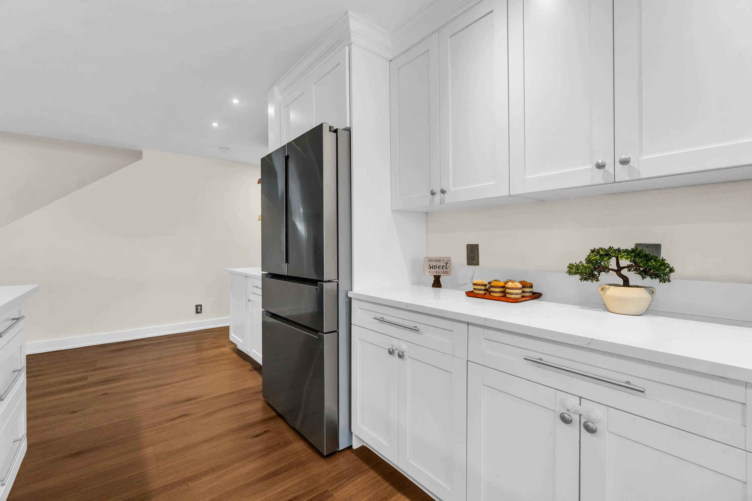 White shaker-style cabinetry with silver hardware, light-toned countertops, and wood-finish flooring