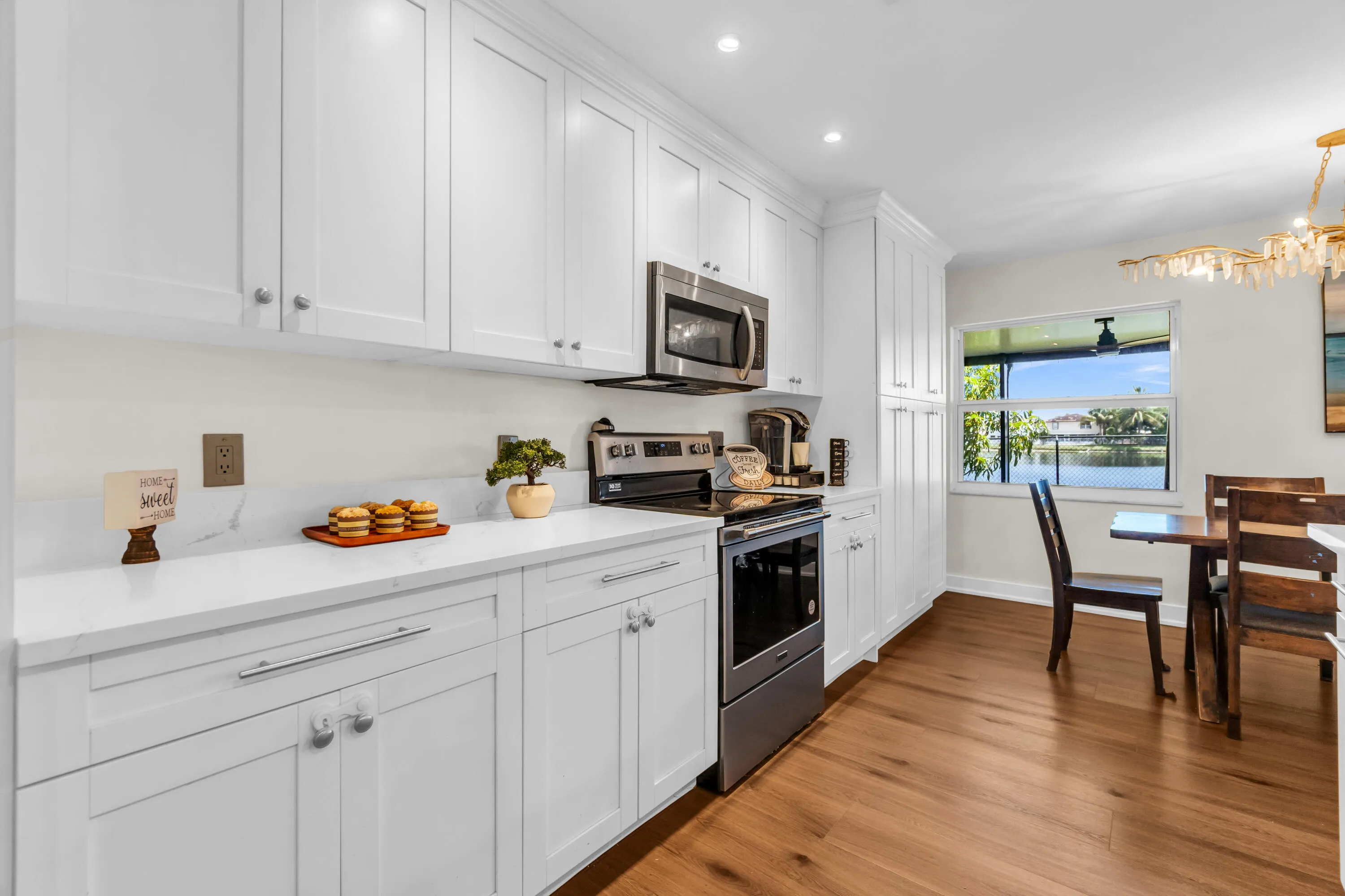 White shaker-style cabinetry with chrome hardware, stainless steel appliances, solid surface countertops, wood-finish flooring, and a large window