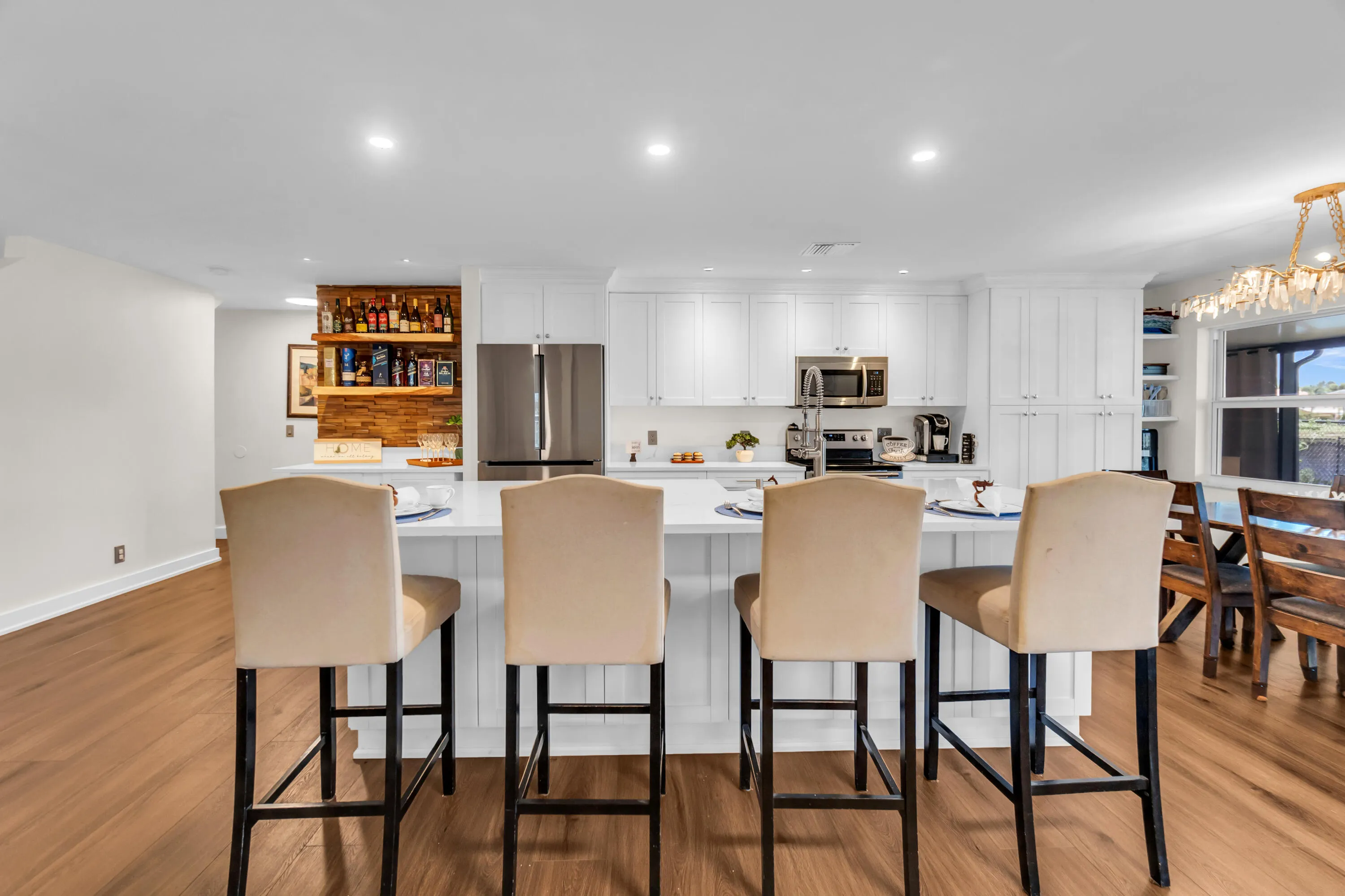 Open-concept kitchen featuring an expansive island with seating, stainless steel appliances, white cabinetry, and wood-finish flooring