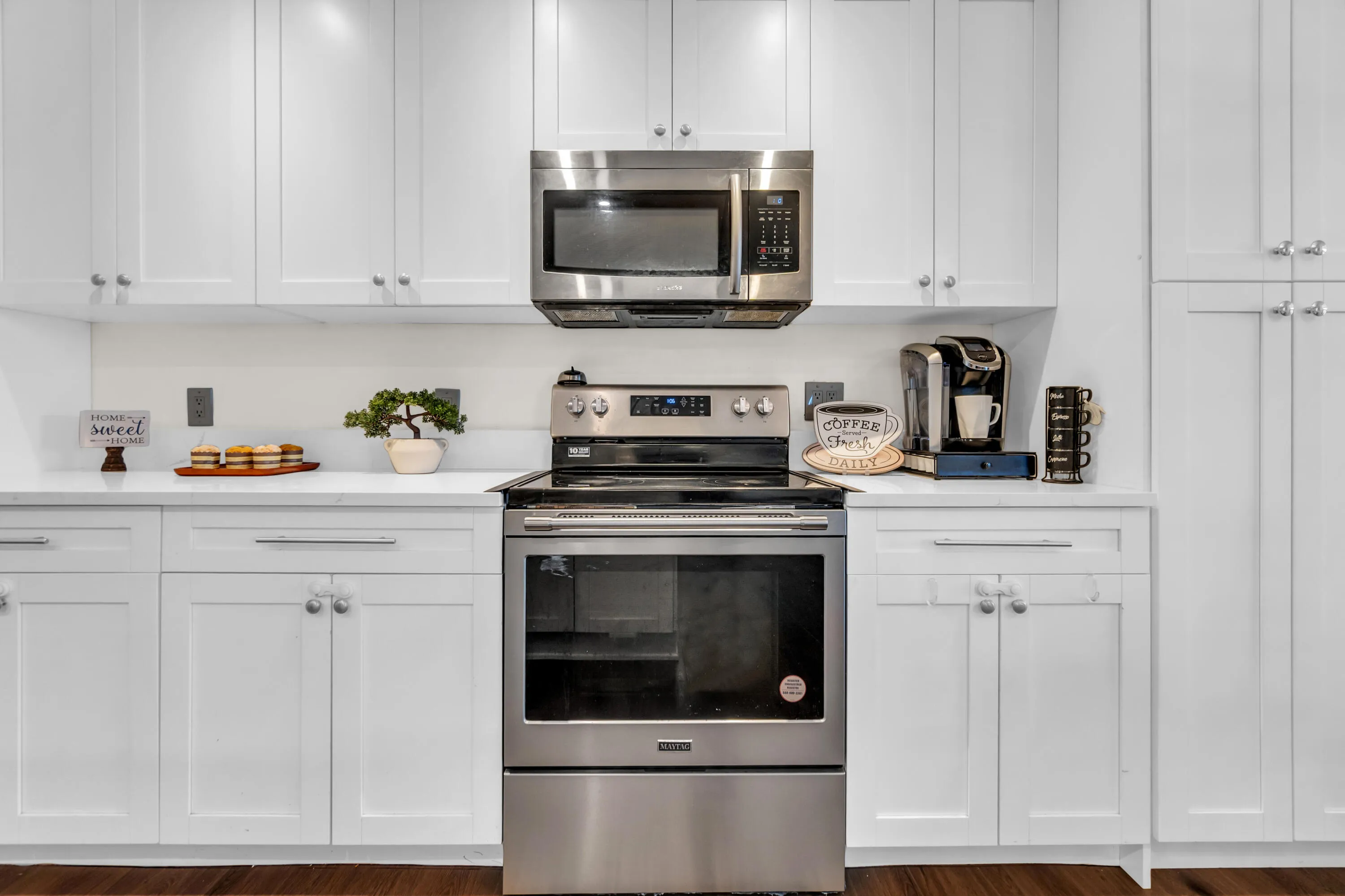 White shaker-style cabinetry, stainless steel appliances, quartz countertops, wood-finish flooring
