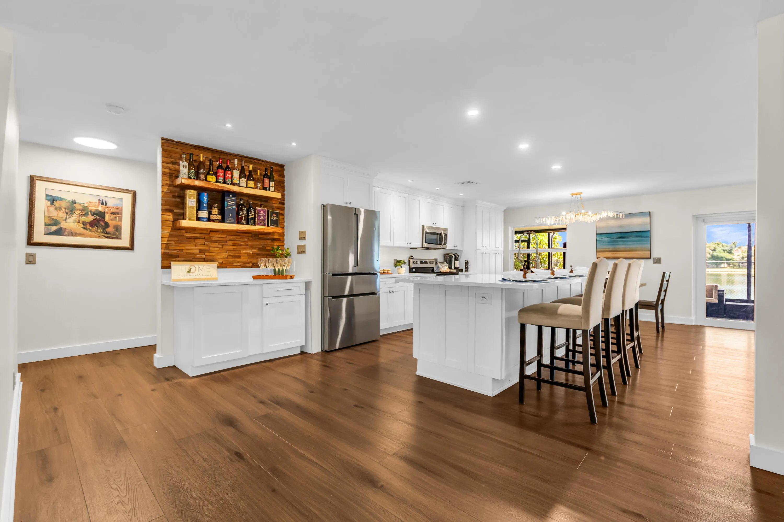 Wide plank wood-finish flooring, white cabinetry, stainless steel appliances, kitchen island with seating, and a built-in beverage bar with wood paneling