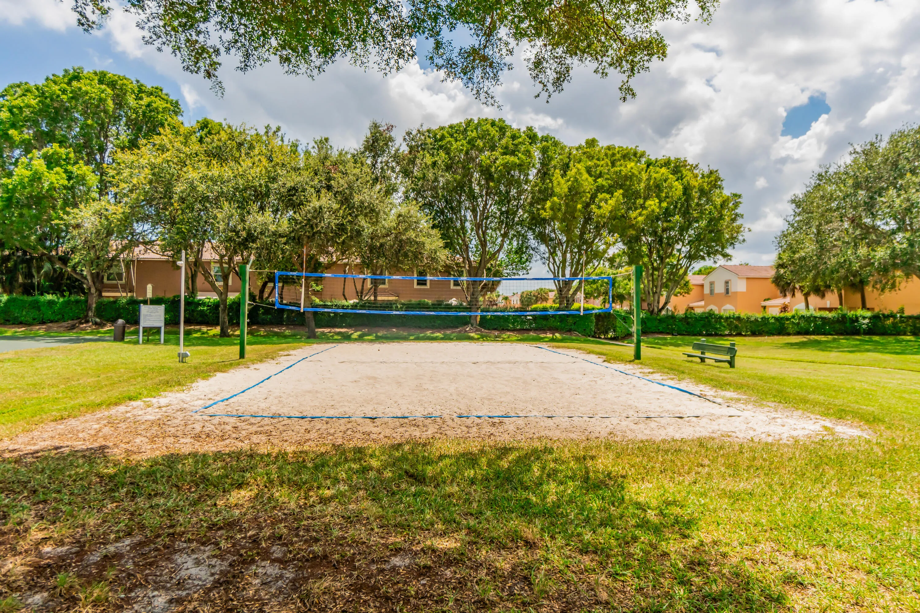Sand volleyball court with a net, bordered by manicured lawn and mature trees