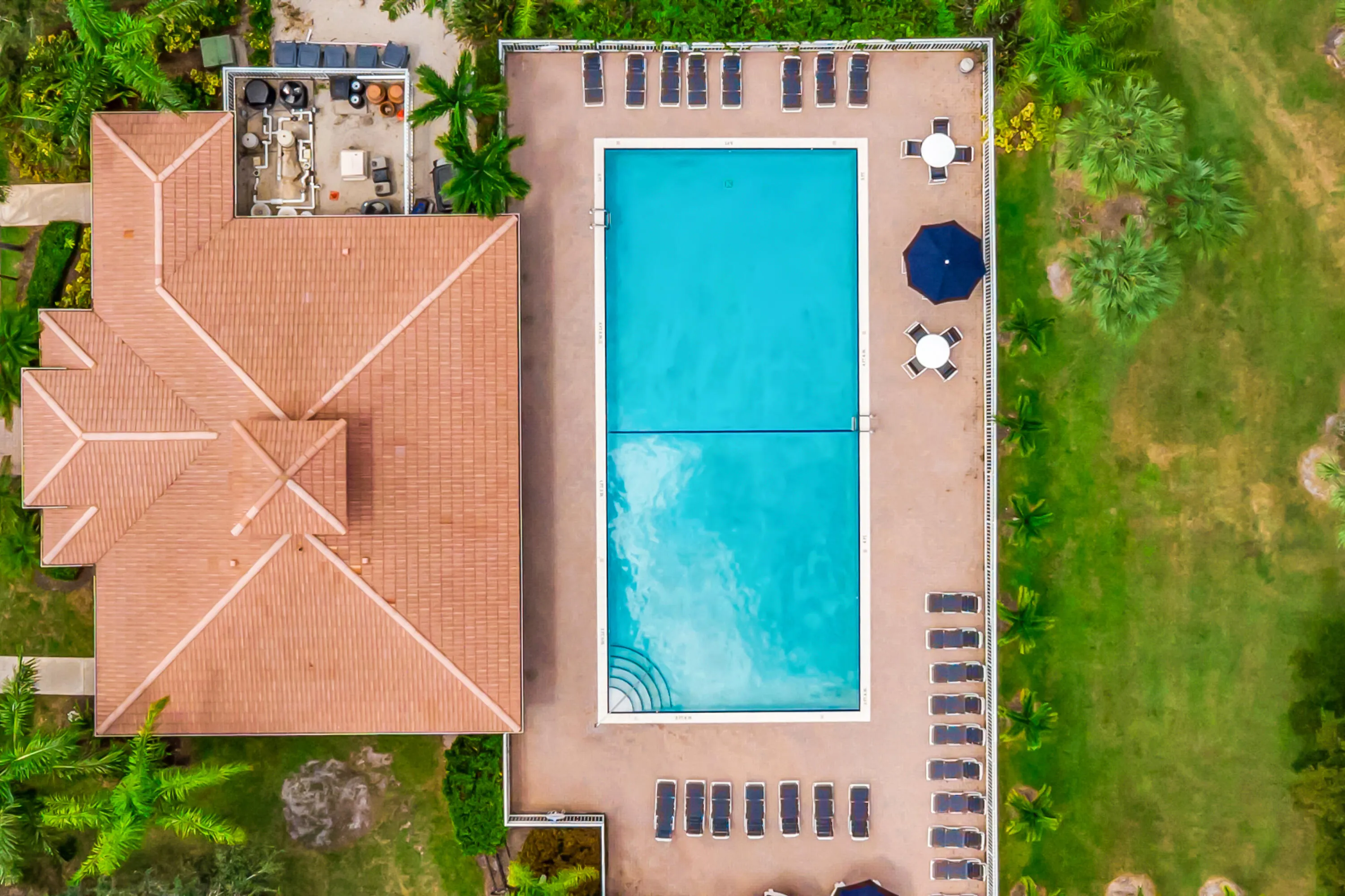 Expansive swimming pool with a surrounding hardscape deck, featuring a multi-tiered tile roof structure and mature tropical landscaping